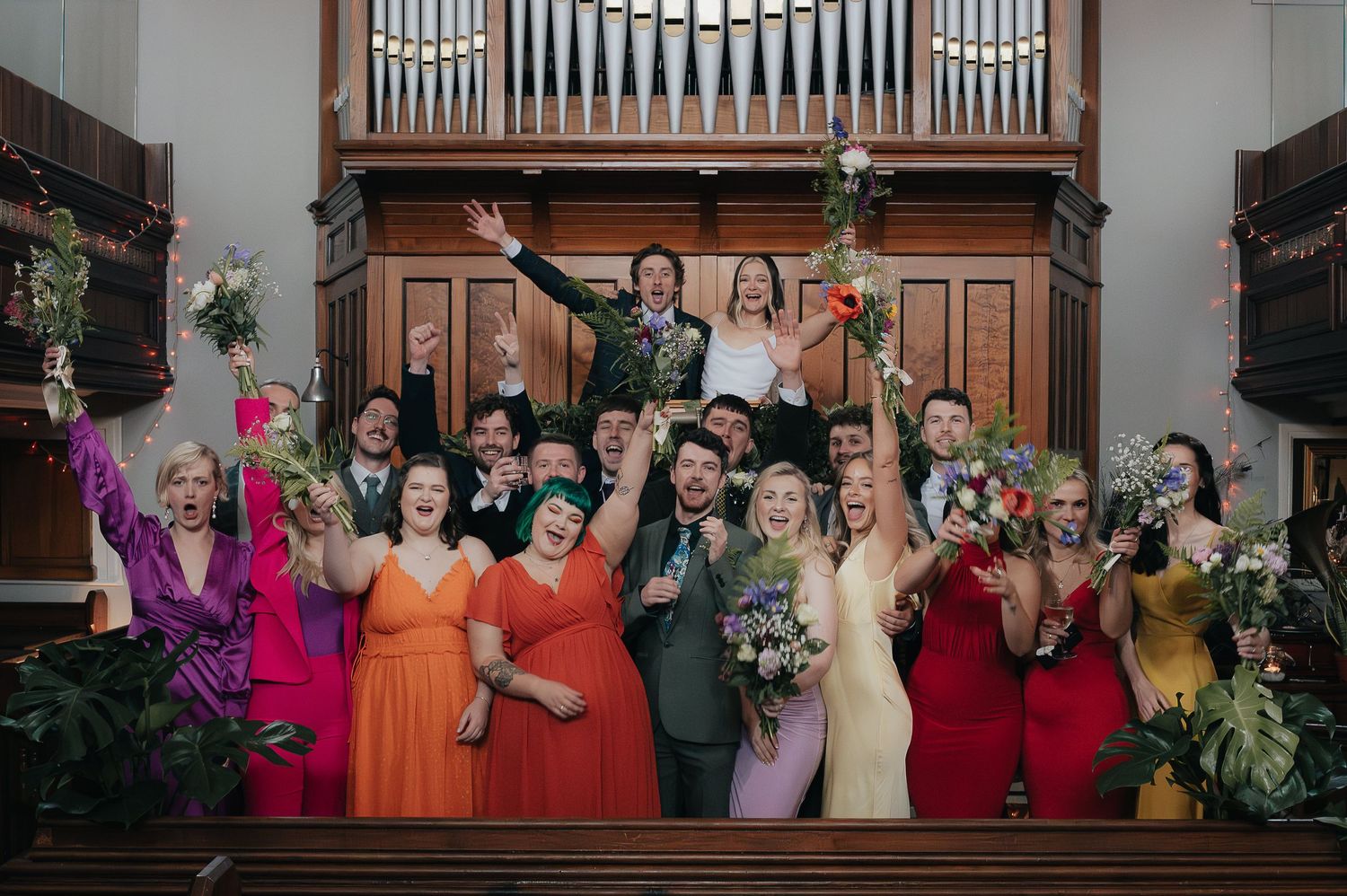 Wedding party posing together on church steps in colorful attire with bouquets.