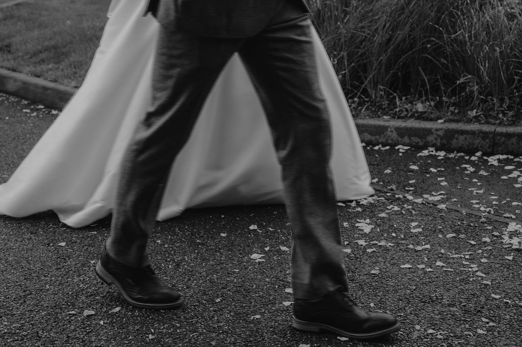 Black and white detail shot of dress and formal shoes walking on outdoor path.