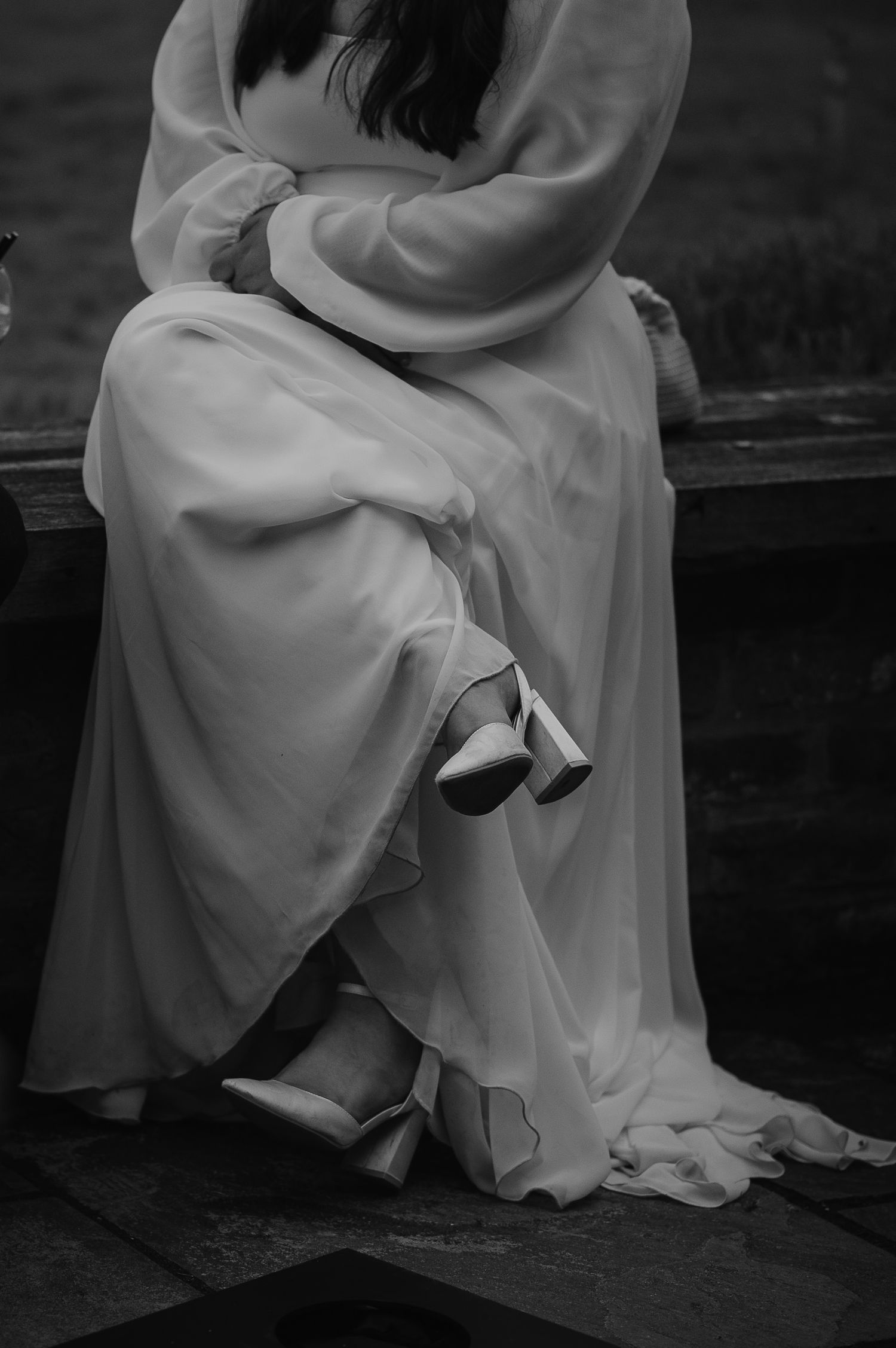 Close-up of a flowing white wedding dress and shoes in black and white.
