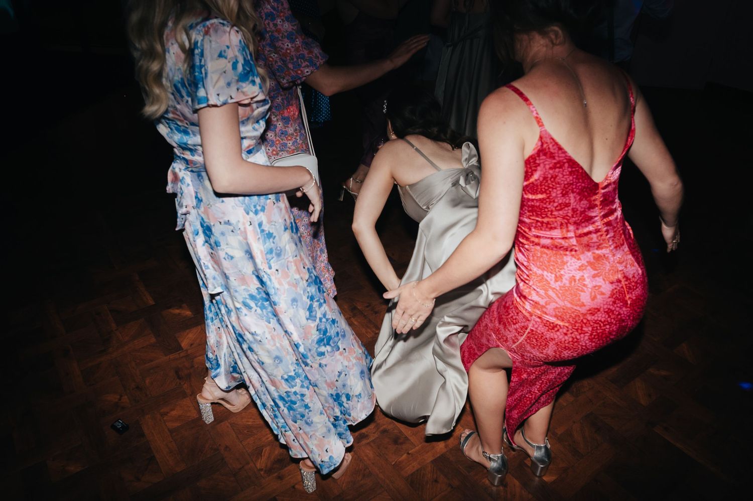 Wedding guests dancing in colorful dresses on a dark dance floor.