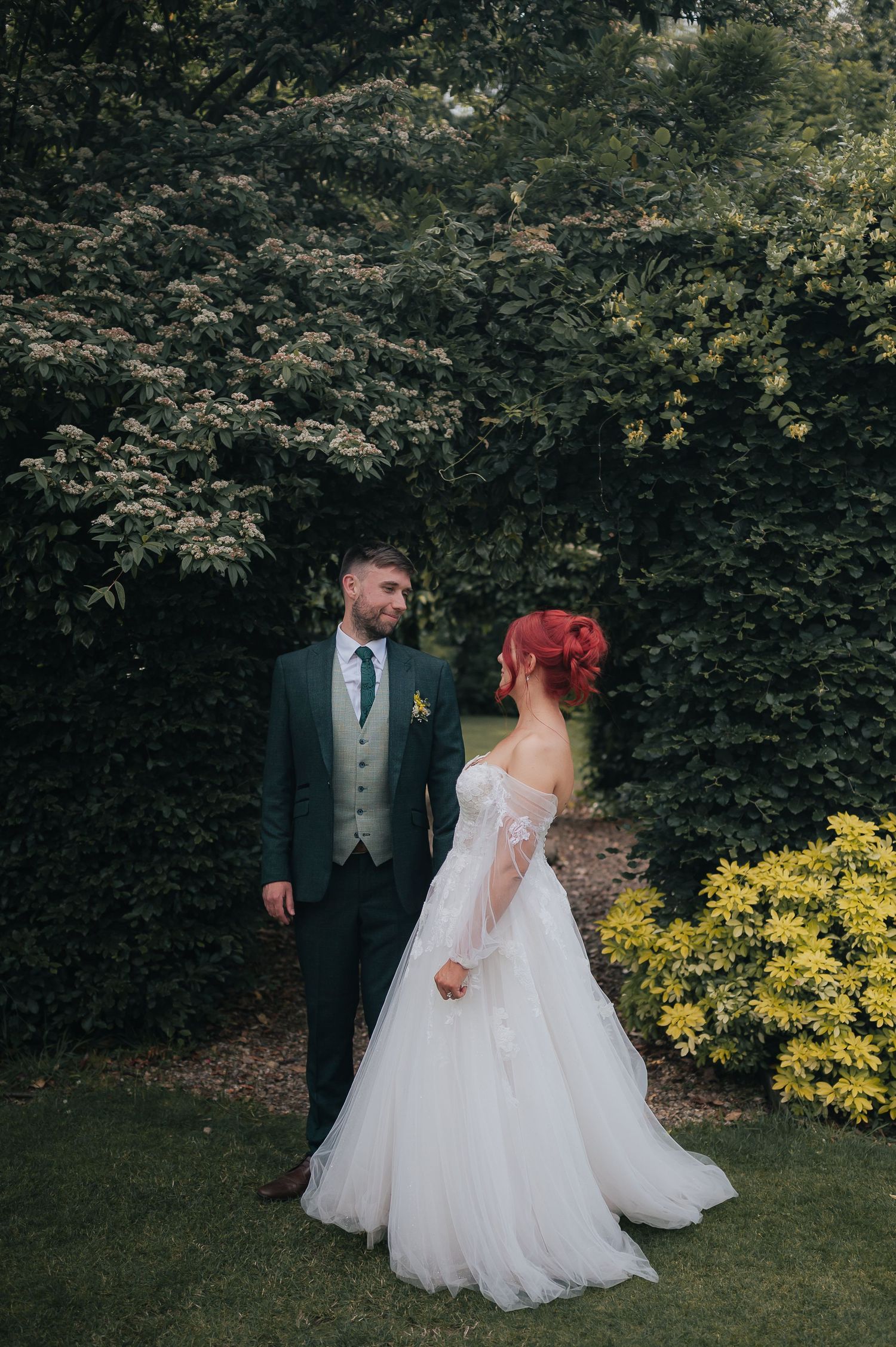Wedding couple poses in garden setting with bride in white dress and distinctive red hair.