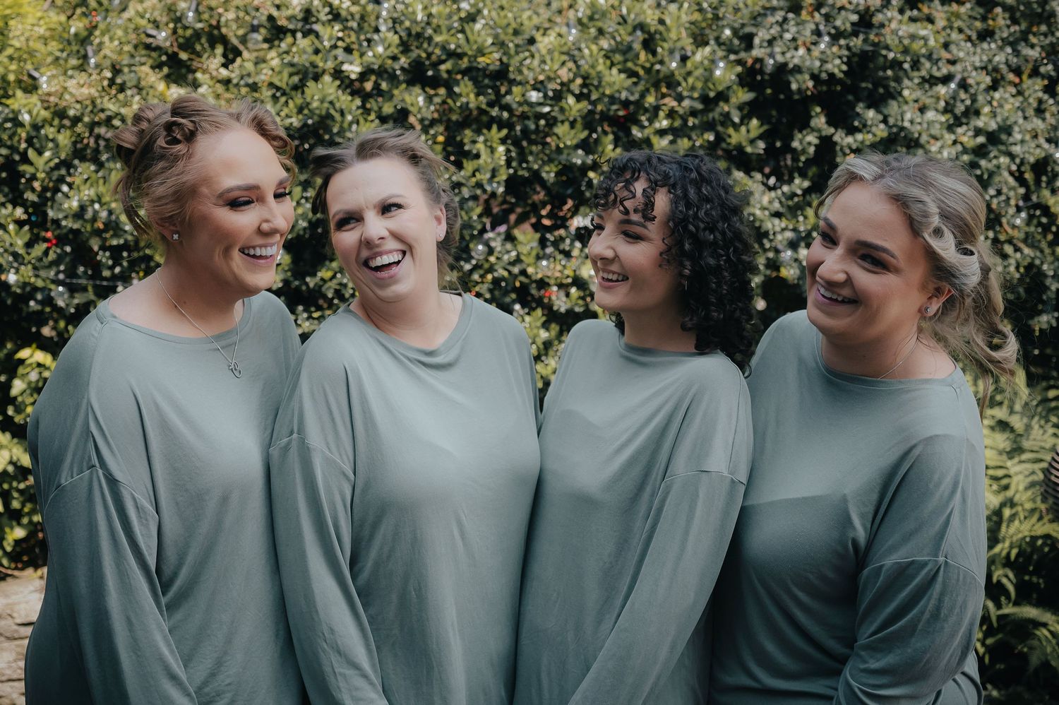 Group wearing matching grey tops poses together outdoors with greenery in background.