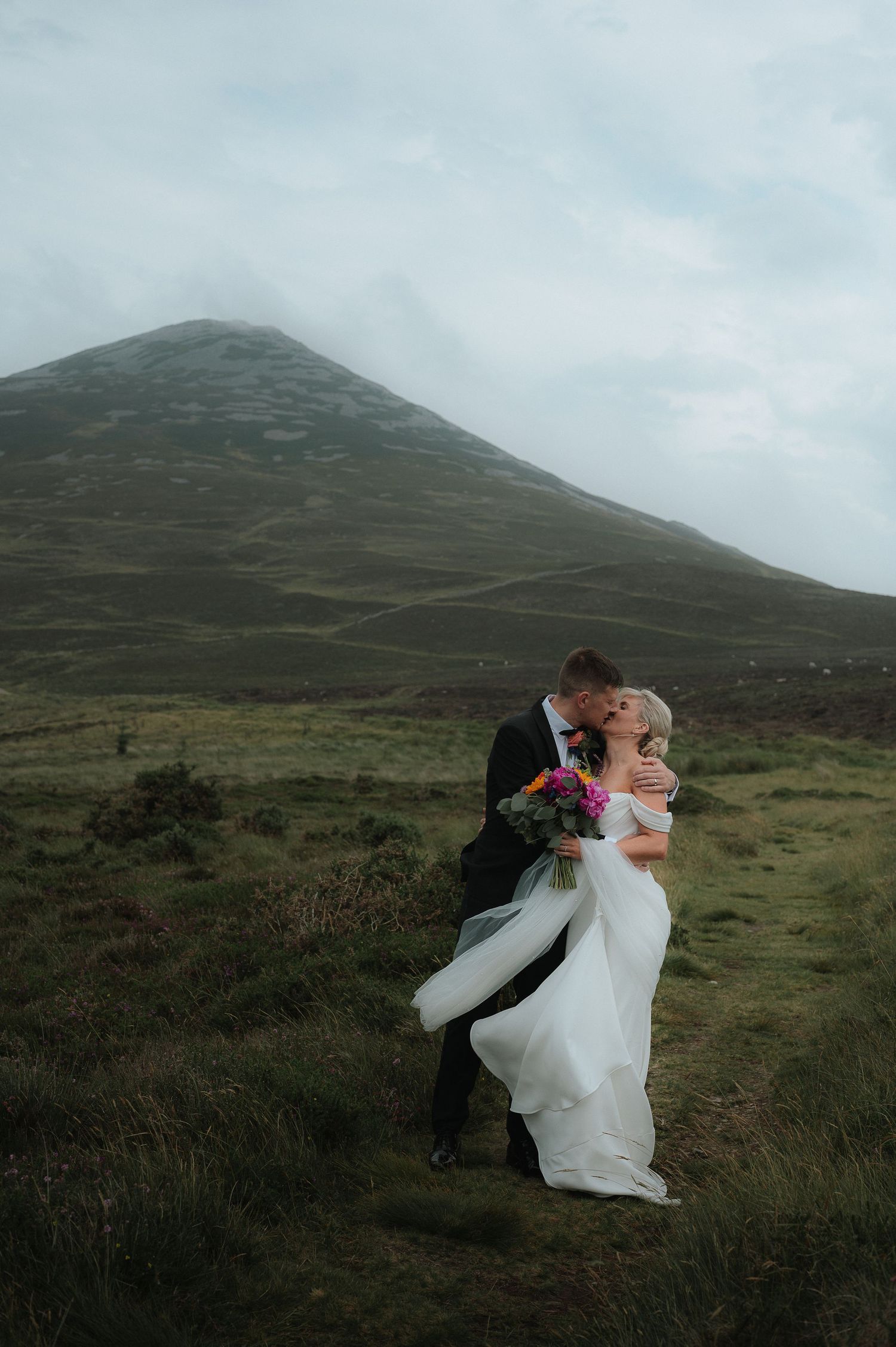 A romantic wedding couple embraces on a misty mountainside with flowing white dress and dramatic landscape. North Wales Wedding Photographer