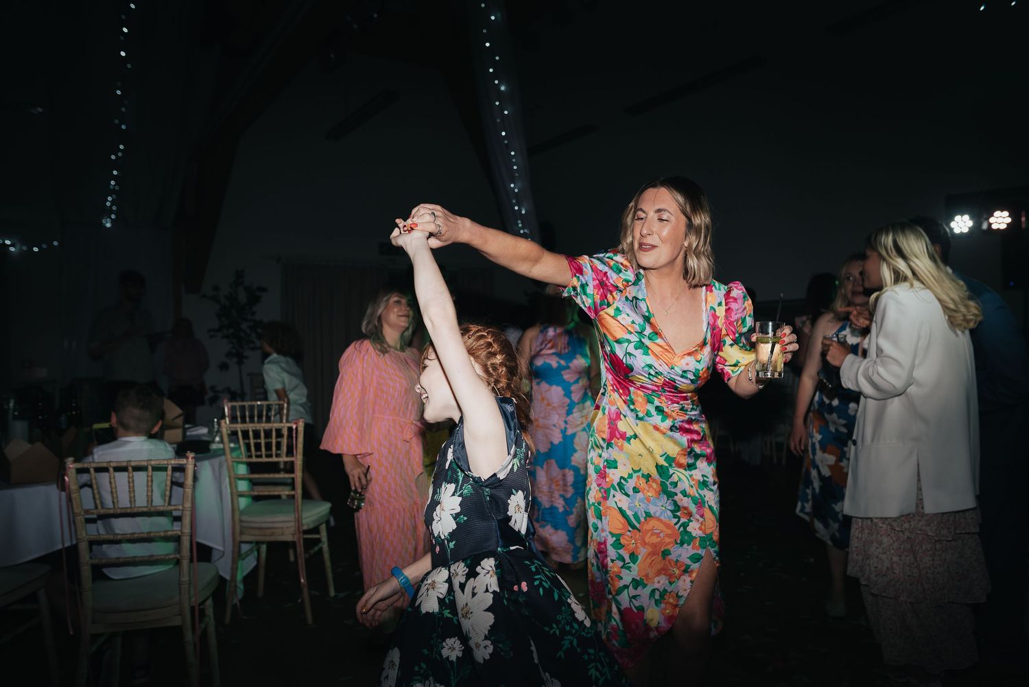Wedding guests dancing and having fun at evening reception with string lights overhead.