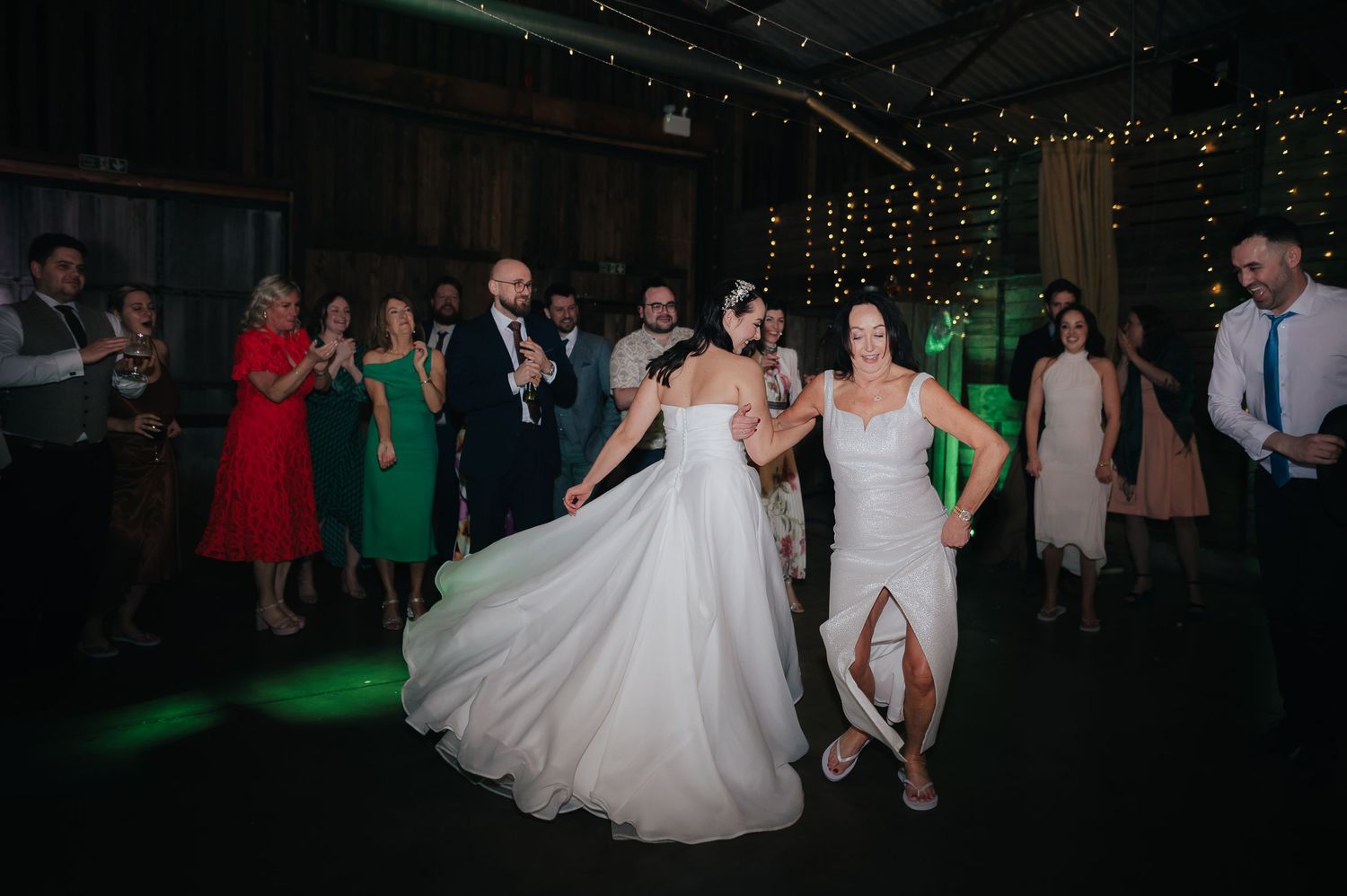 Couples and guests dancing at a wedding reception under twinkling lights with green and red dresses.