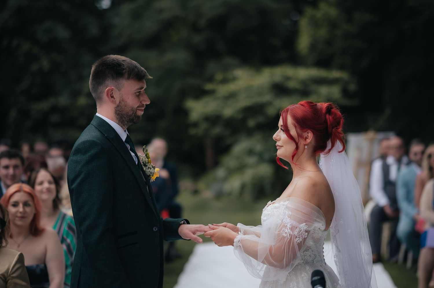 A wedding ceremony taking place outdoors with guests visible in the background.