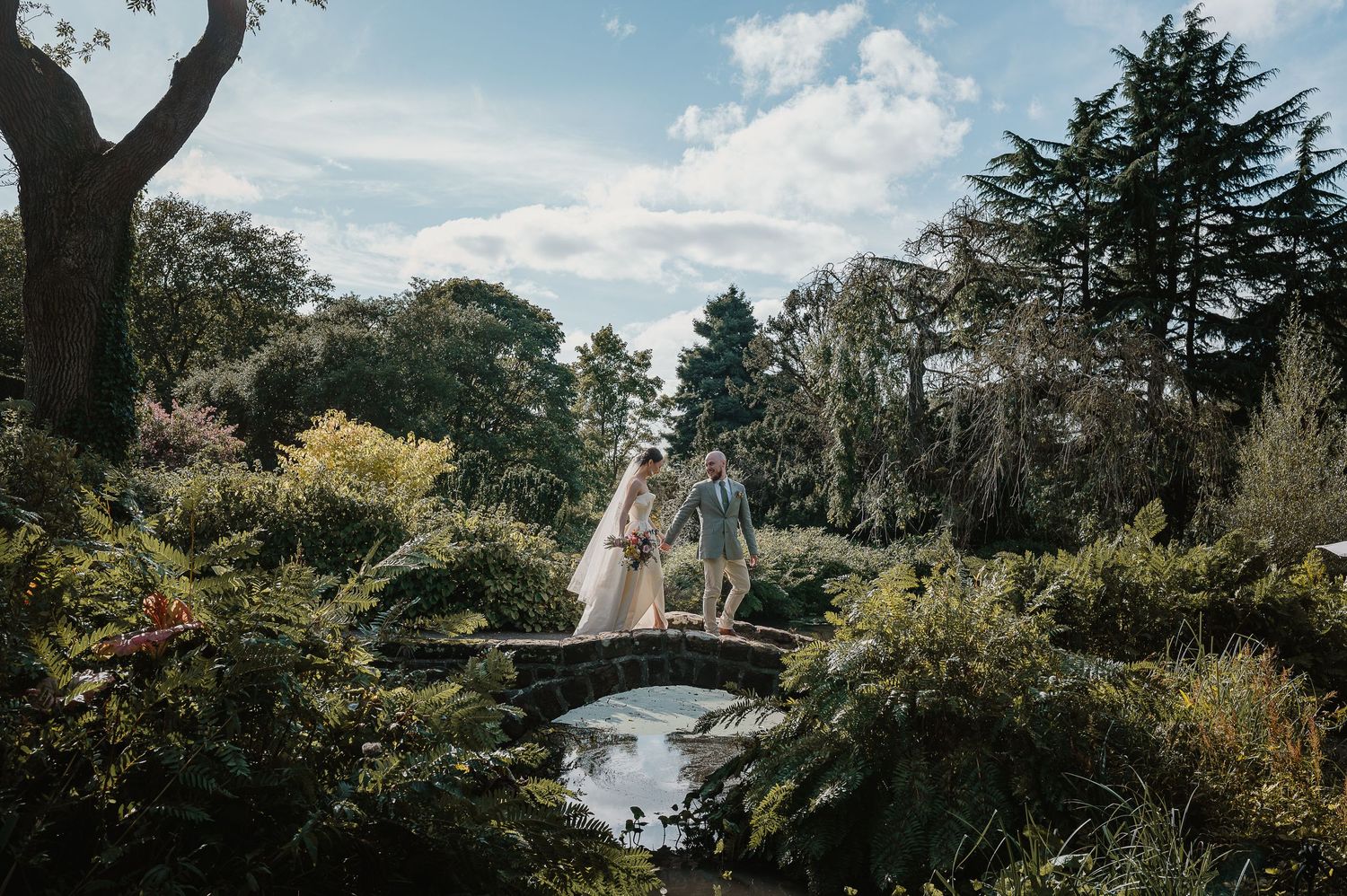 A couple crosses a charming garden bridge during their wedding photography session.
