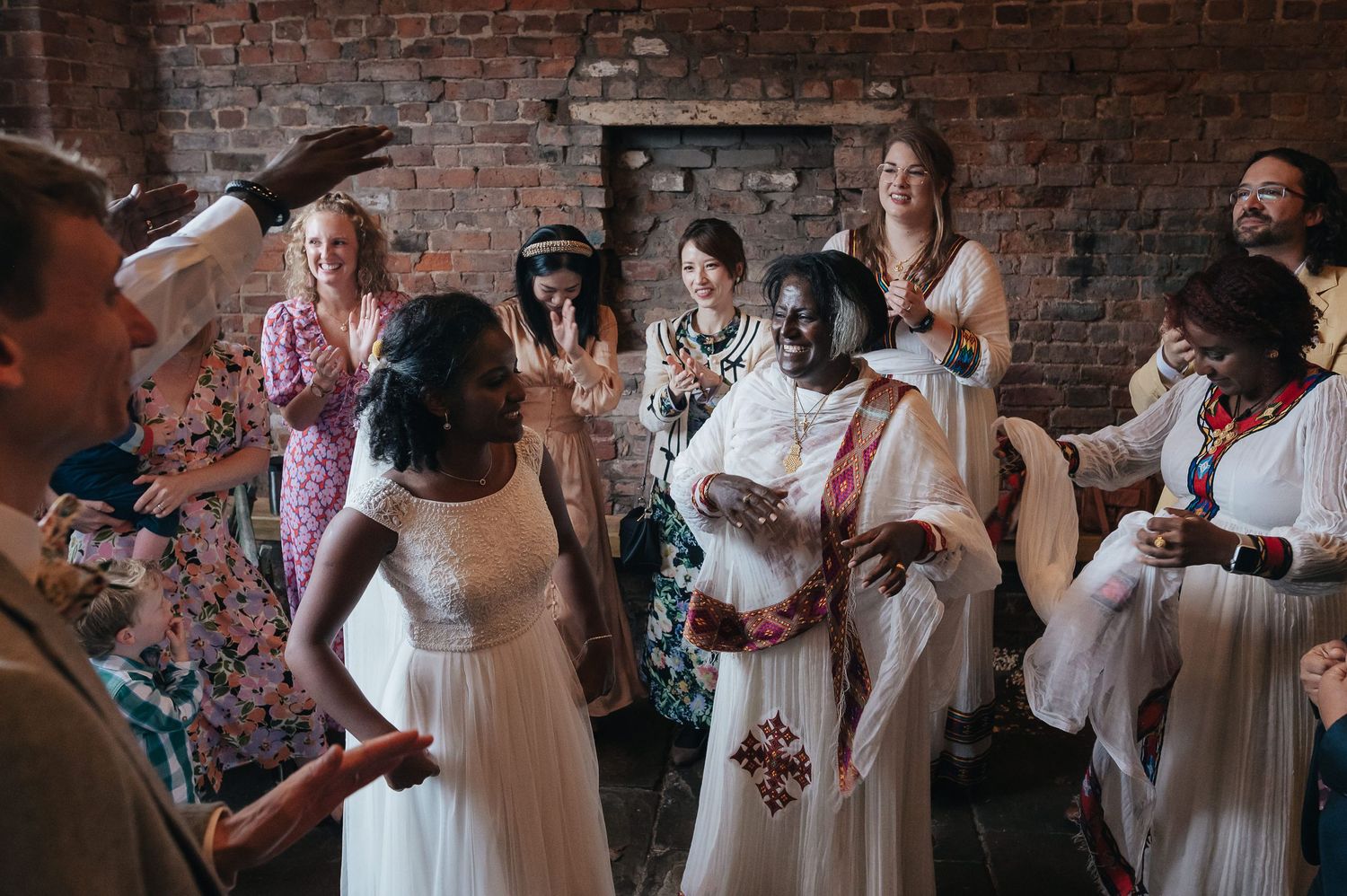 A group in white dresses gathered for a celebratory moment in a brick-walled venue.