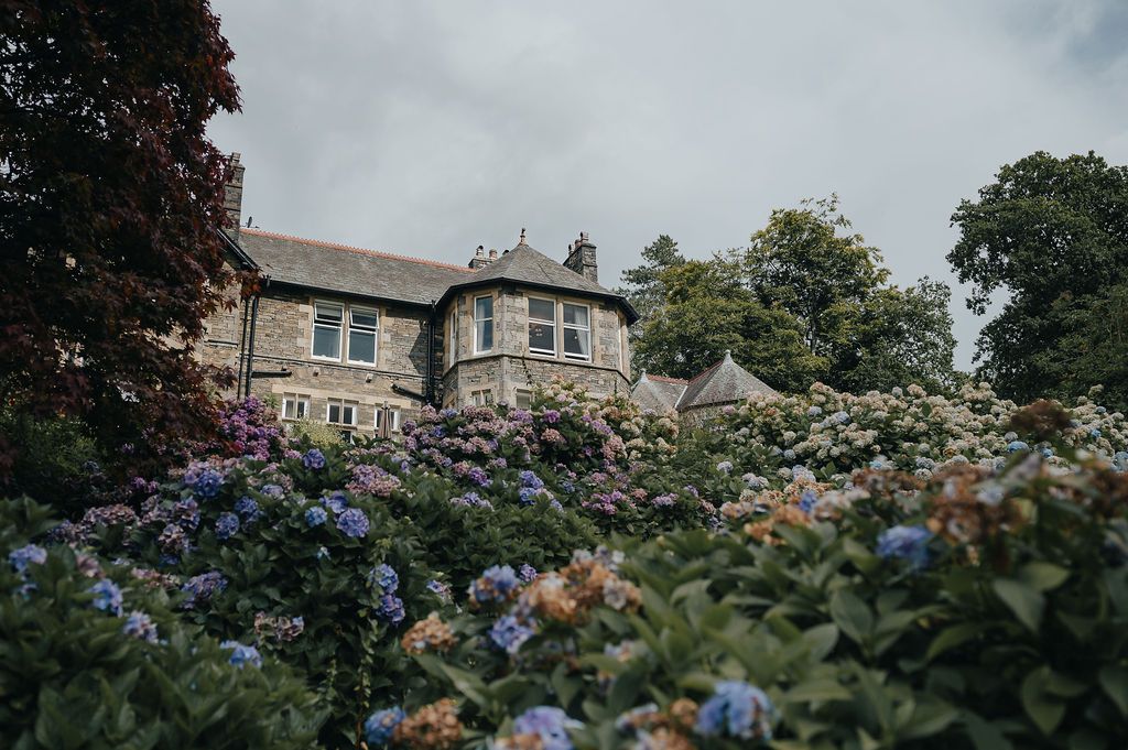 Historic stone manor house with blooming hydrangea garden in the foreground.