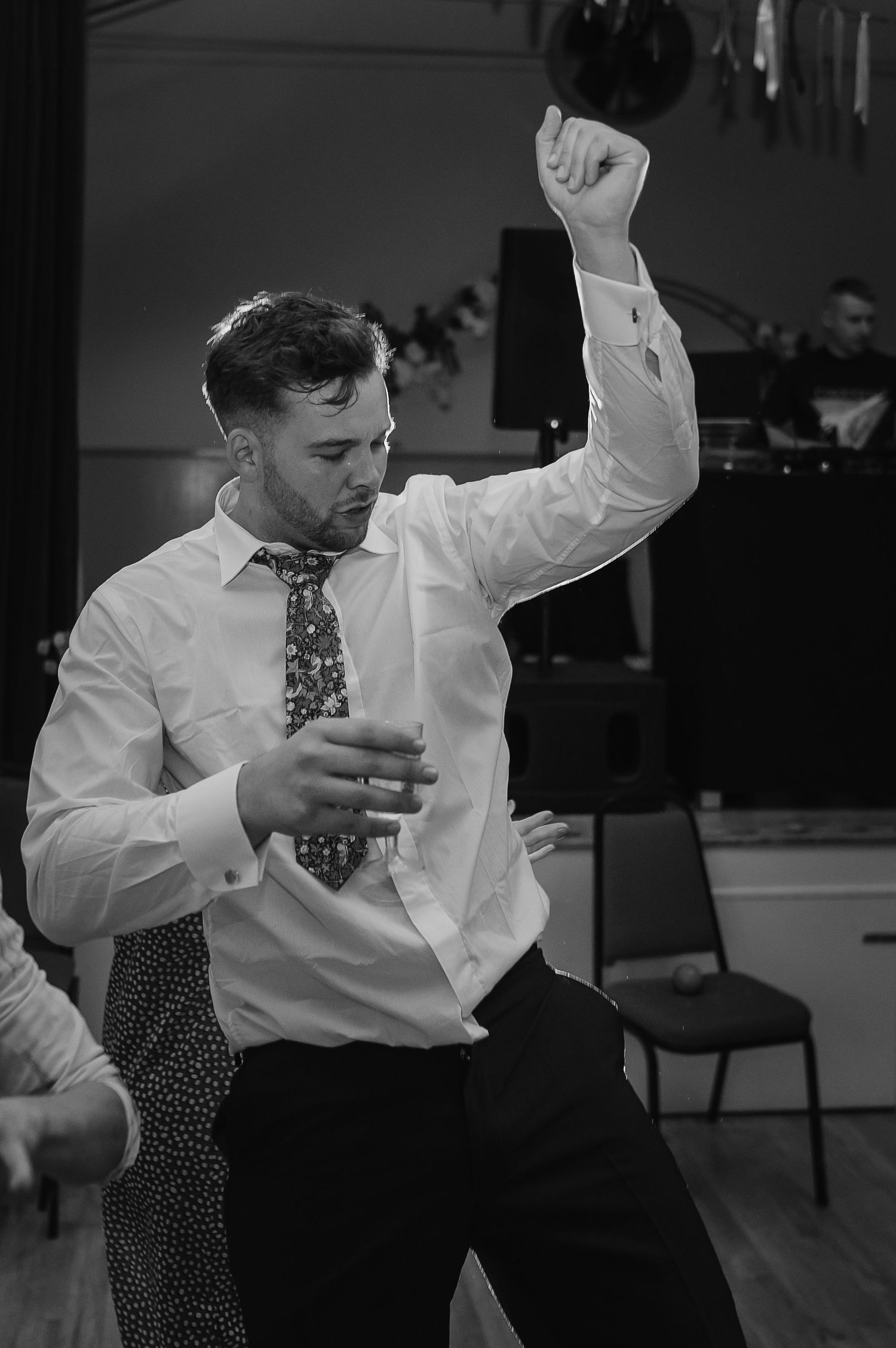 A man in a white dress shirt and tie dances enthusiastically with one arm raised at a party event.