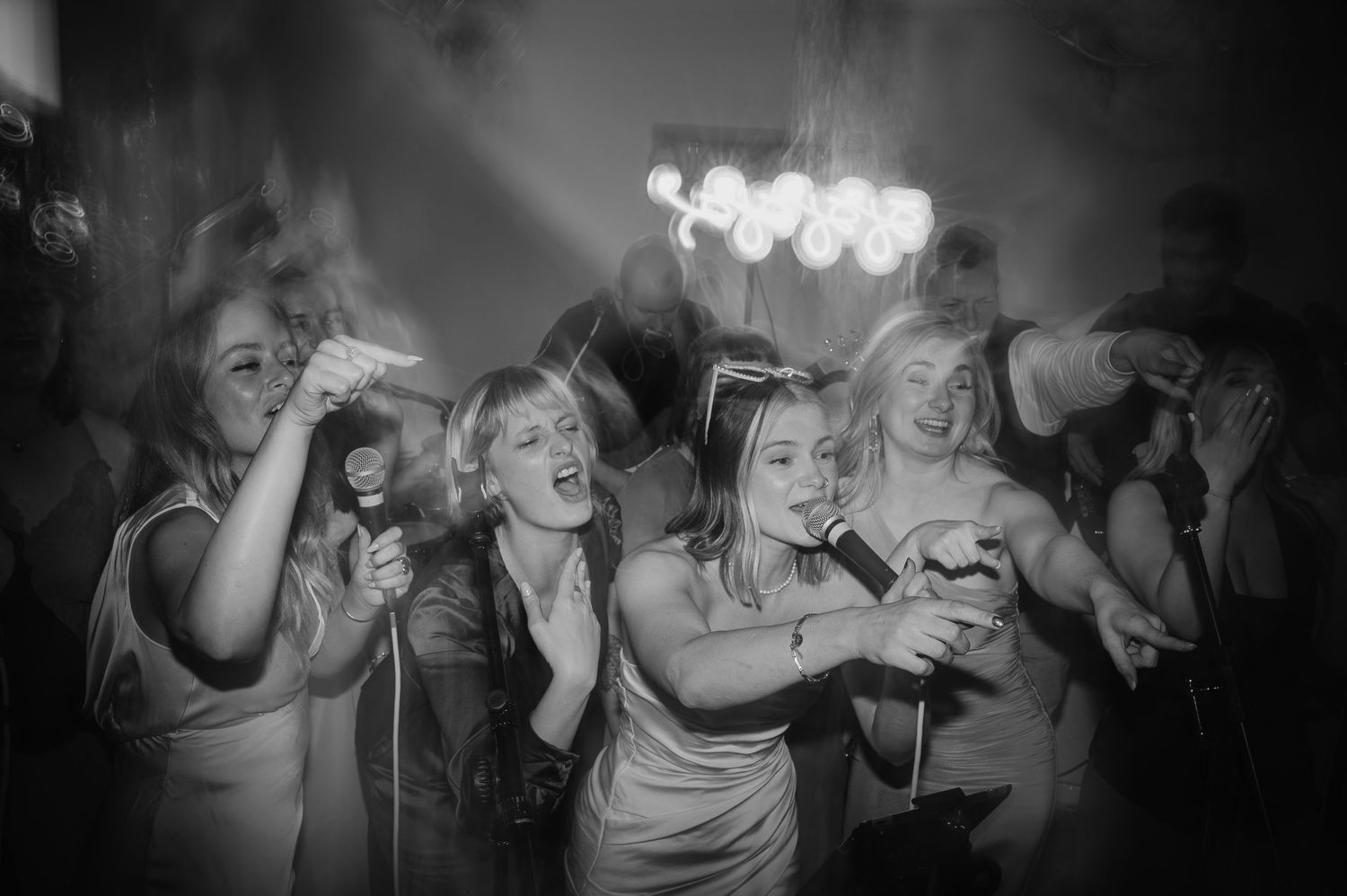 Black and white photo of dancing wedding guests celebrating under ambient lighting.