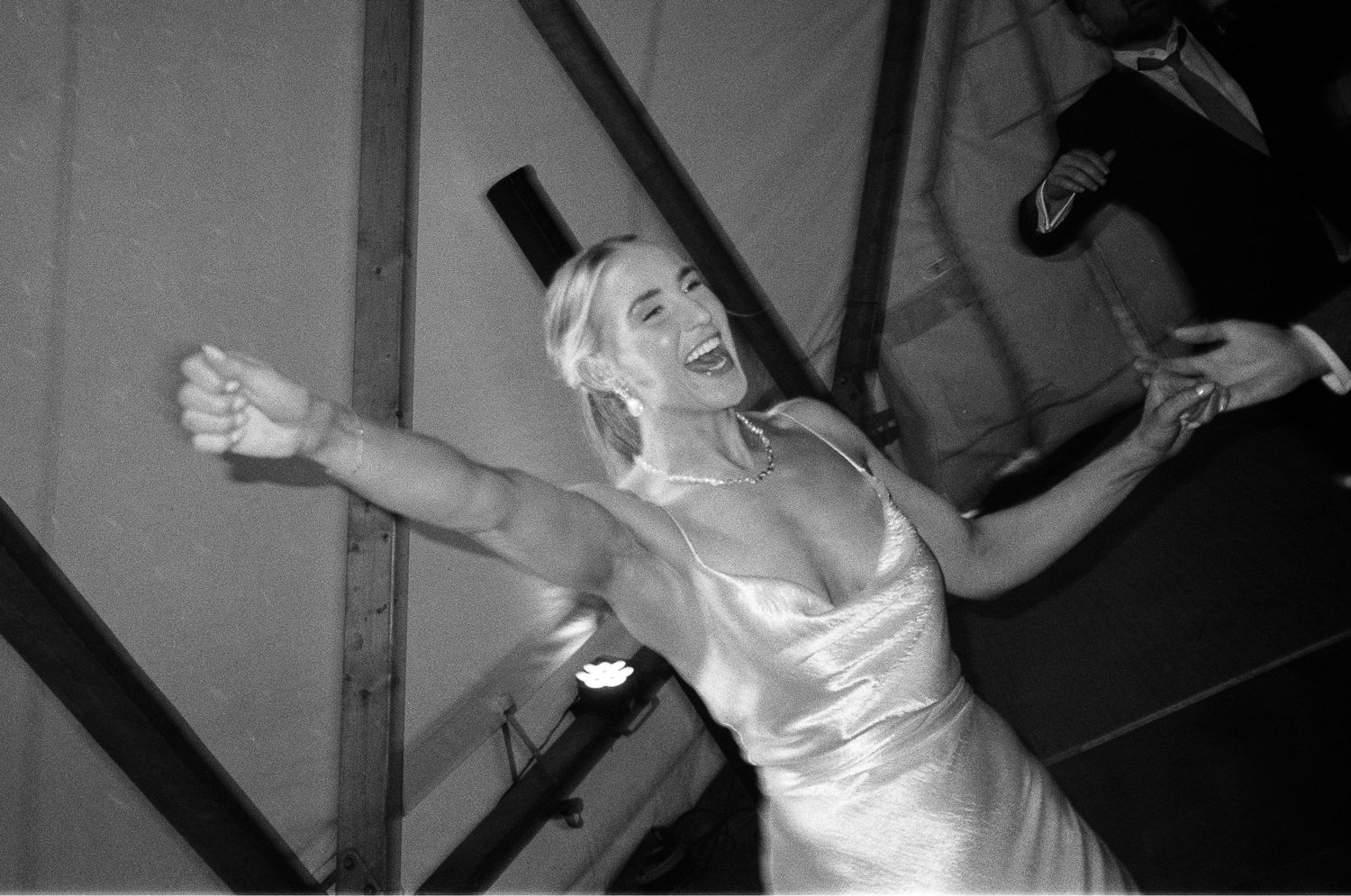 Black and white photo of a joyful blonde woman in a satin dress dancing with arms outstretched at an event.