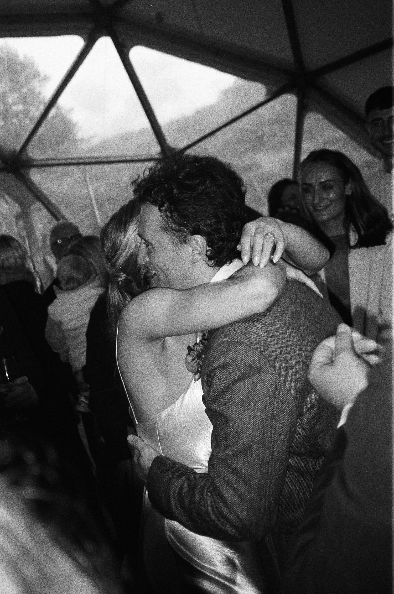 Black and white photo of a couple sharing a first dance embrace at a wedding reception under a tent.