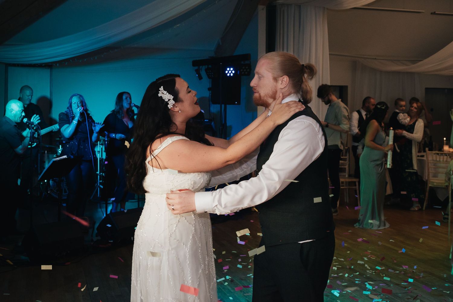 A couple dances together at their wedding reception under blue ambient lighting.