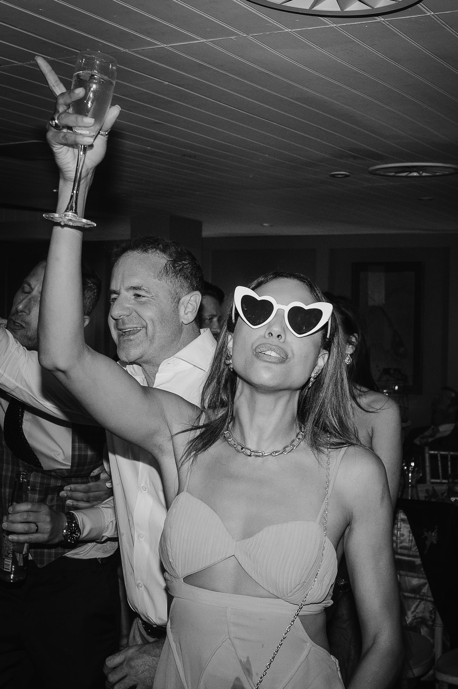 Party scene with someone wearing heart-shaped sunglasses and raising champagne glass in celebration.