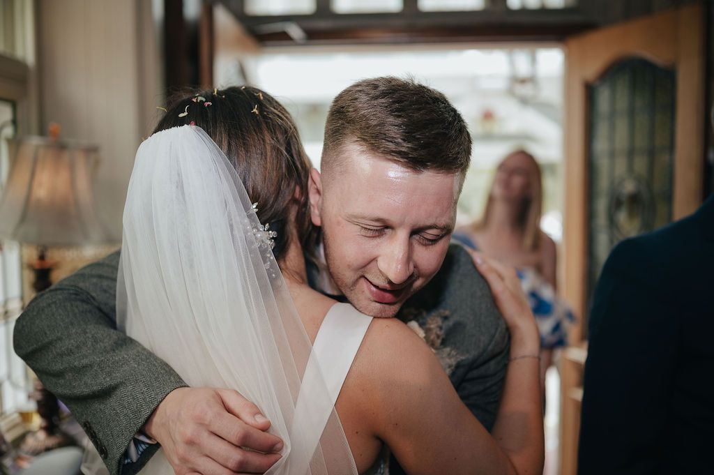 An emotional embrace shared between a bride in white veil and a suited figure during a wedding ceremony.