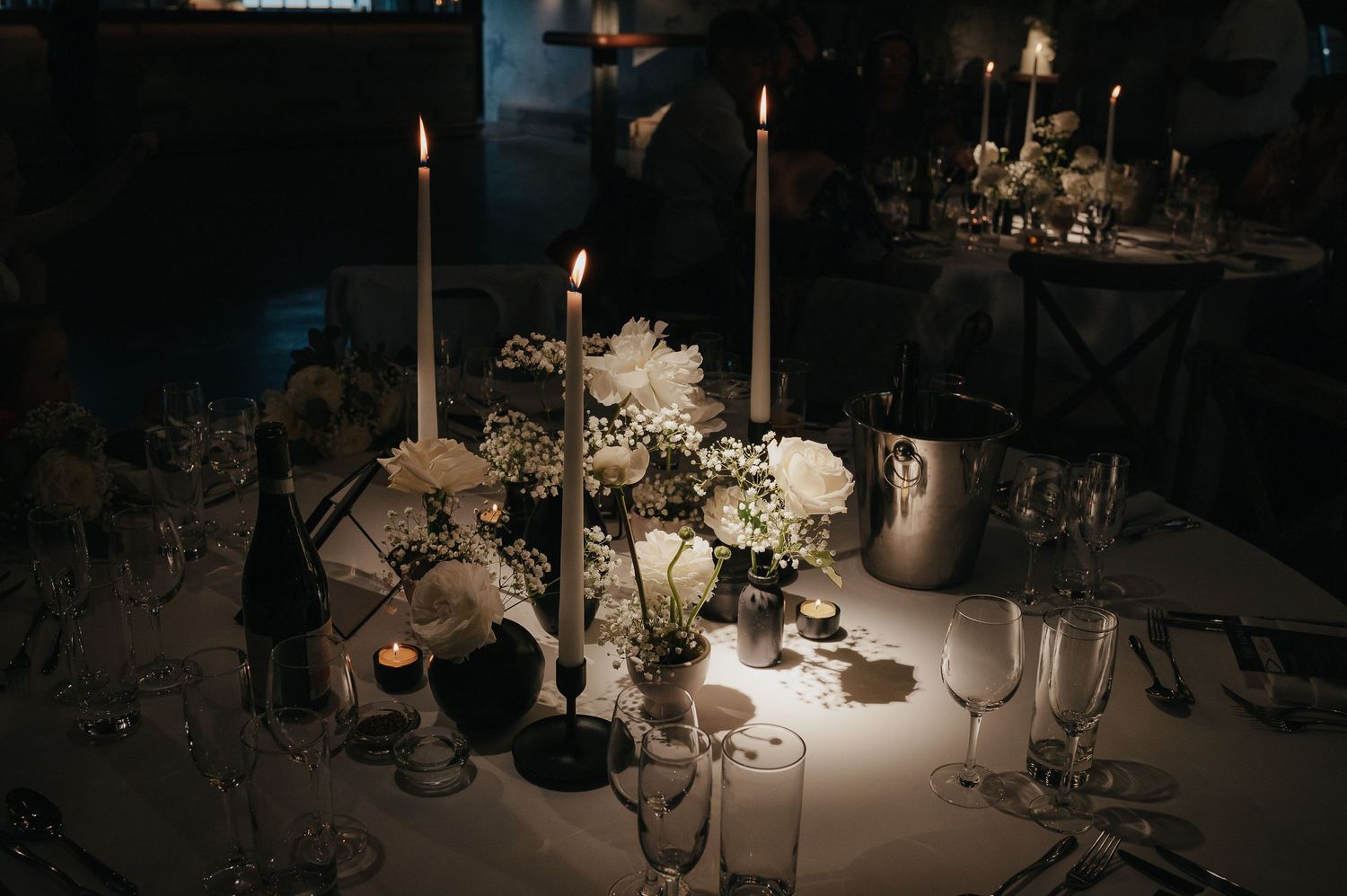 Elegant candlelit wedding table setting with flowers and glassware in moody lighting.