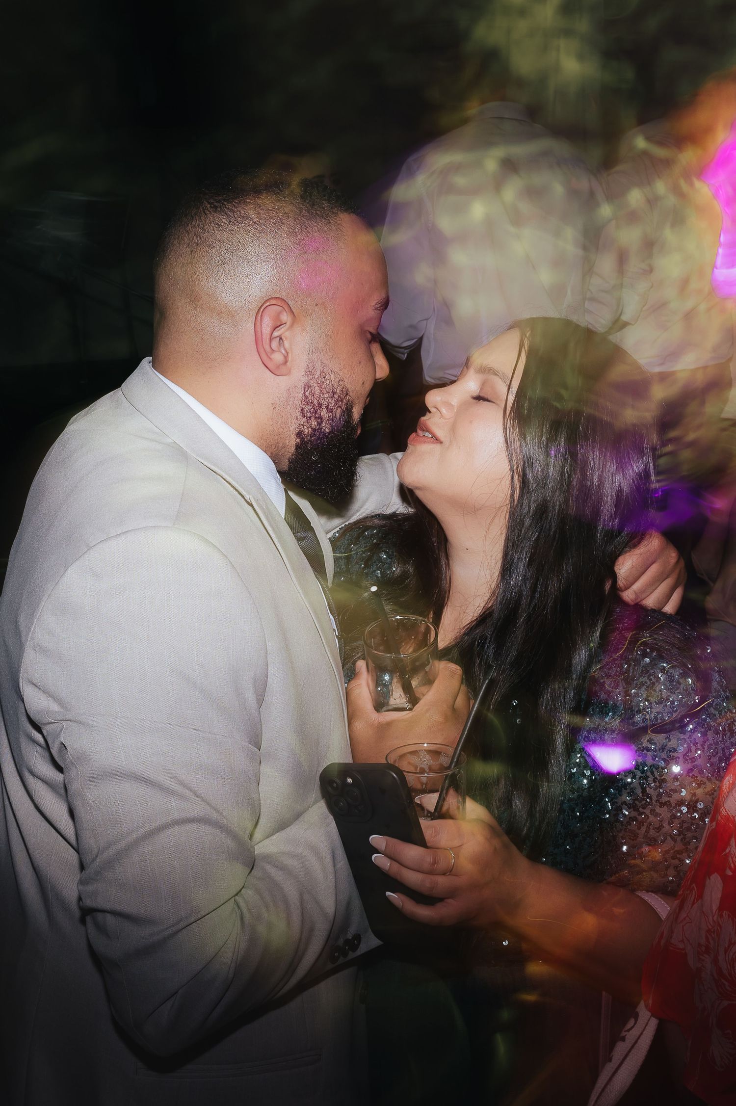 A romantic moment between a couple sharing an intimate dance at a party with colorful lights and smoke effects.