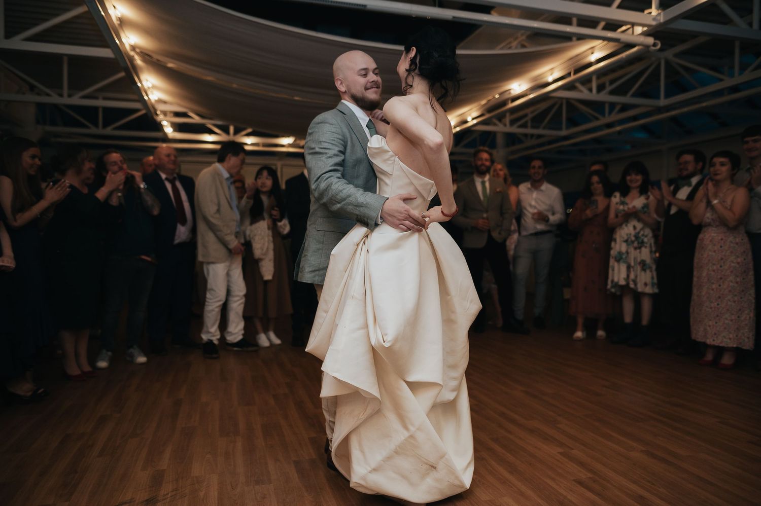 Couple dances together during wedding reception on wooden dance floor.