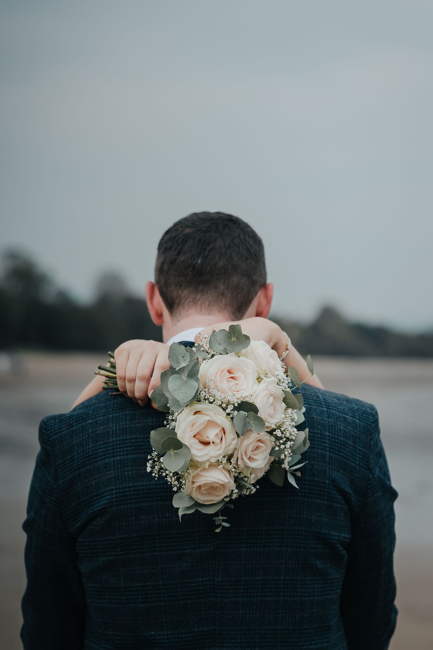 A close-up view of pink roses and eucalyptus bouquet held against a navy suit jacket.