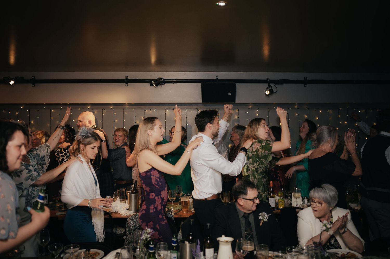 Wedding reception celebration with guests dancing and celebrating at decorated indoor venue.