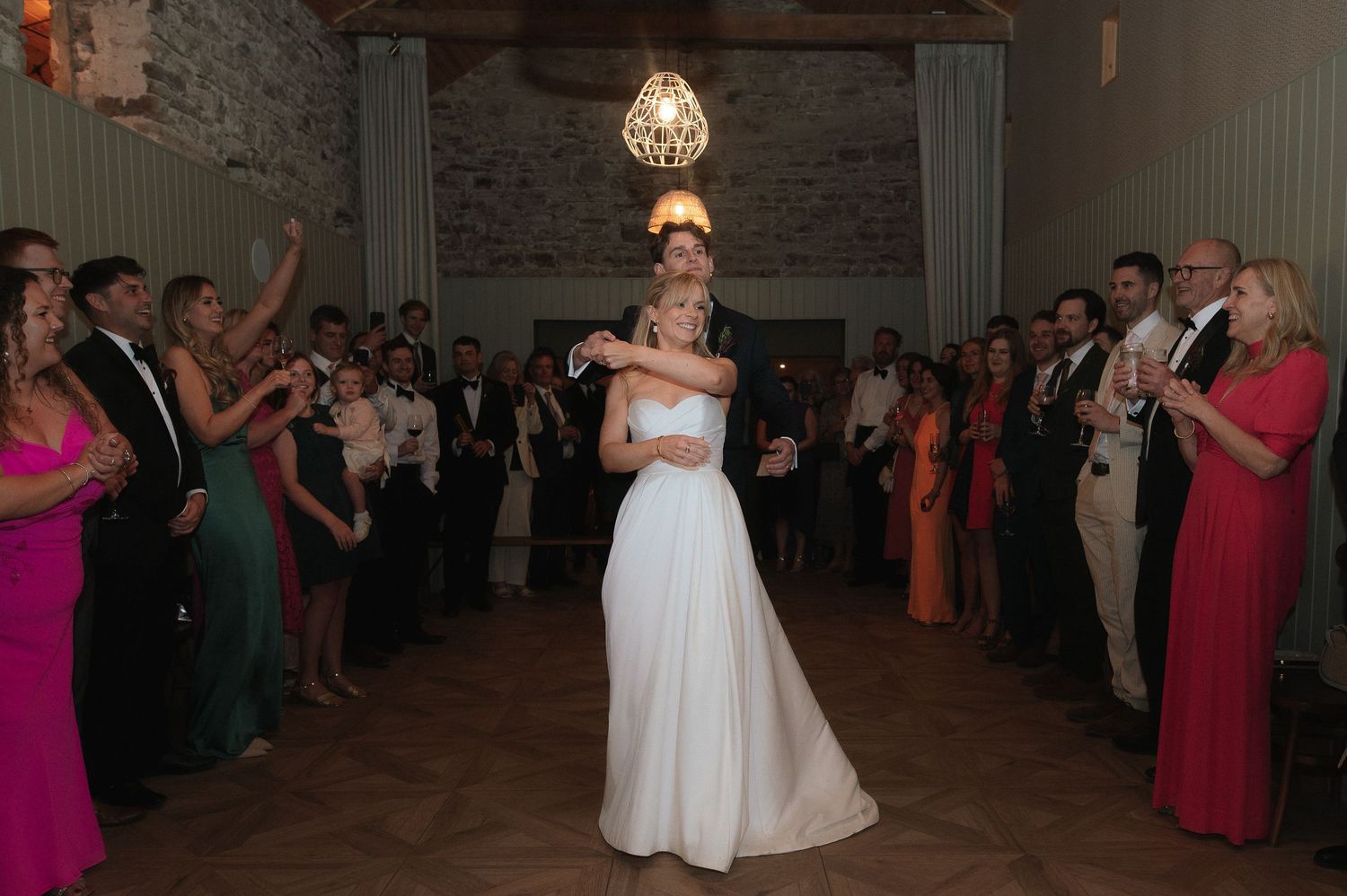 Wedding reception dance floor scene in an elegant ballroom with crystal chandeliers and guests looking on.