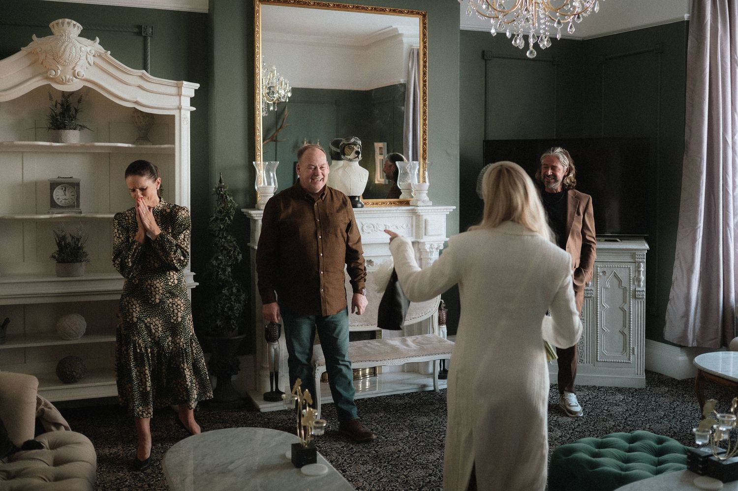 A cinematic sequence showing multiple angles of a dimly lit elegant room with a chandelier and green tufted furniture.