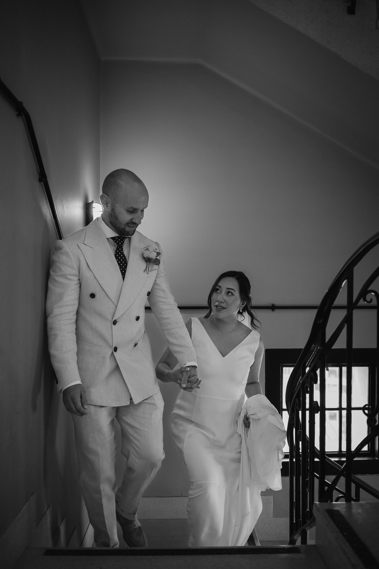 A black and white image of newlyweds ascending a curved staircase together.