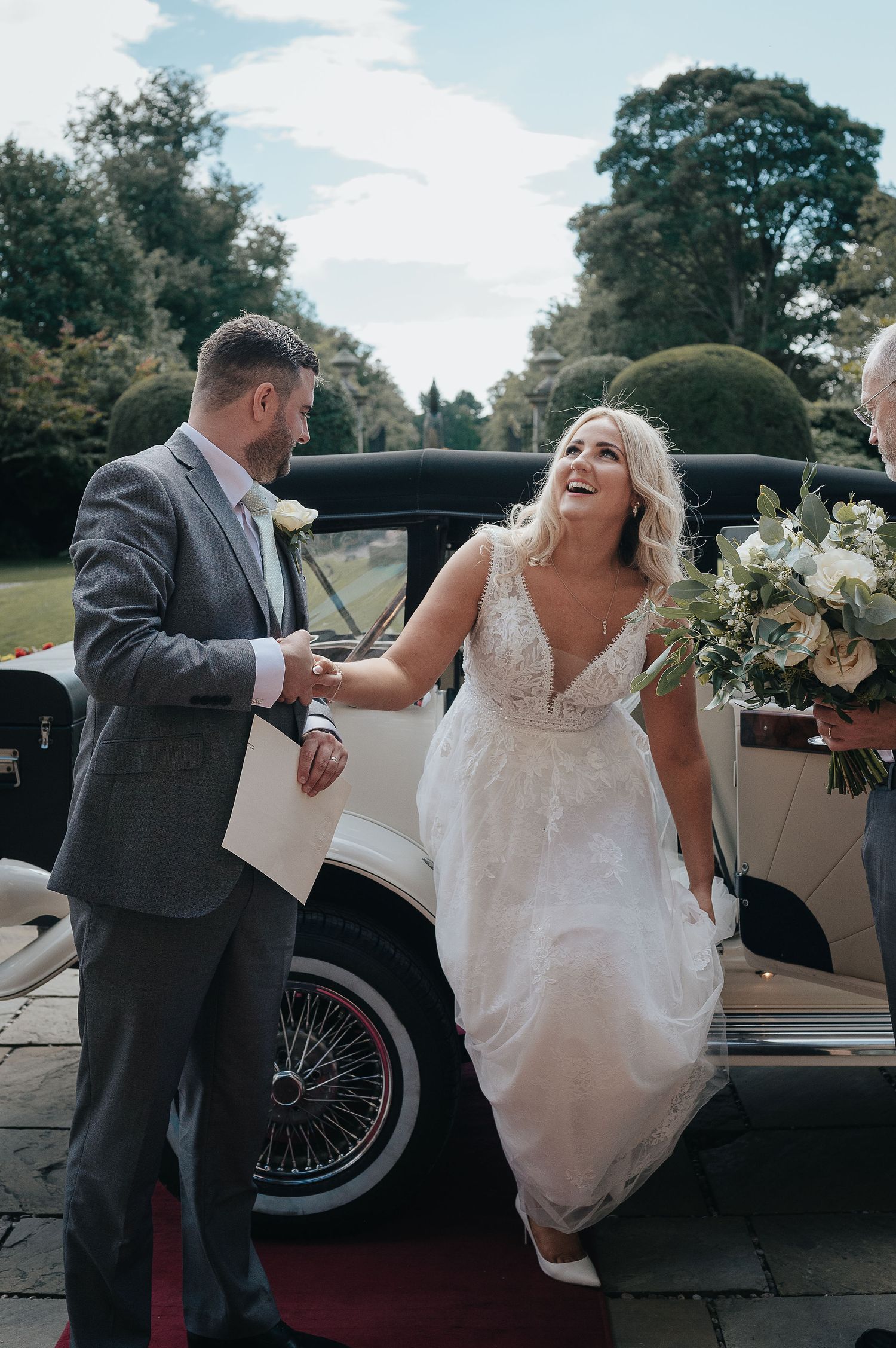 Joyful moment between newlyweds next to a classic vintage car on their wedding day.