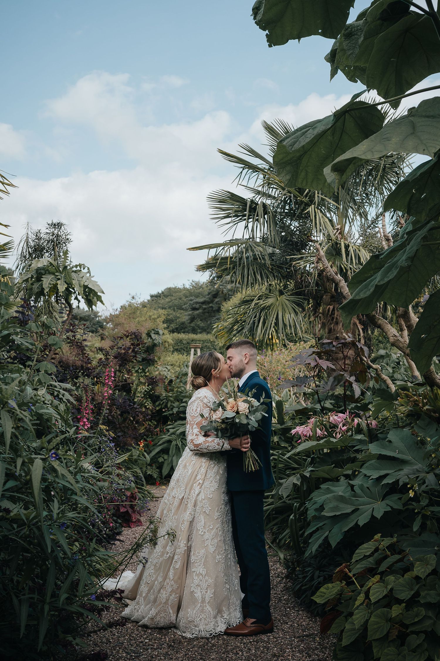 Couple embracing on garden path surrounded by tropical plants and palm trees.