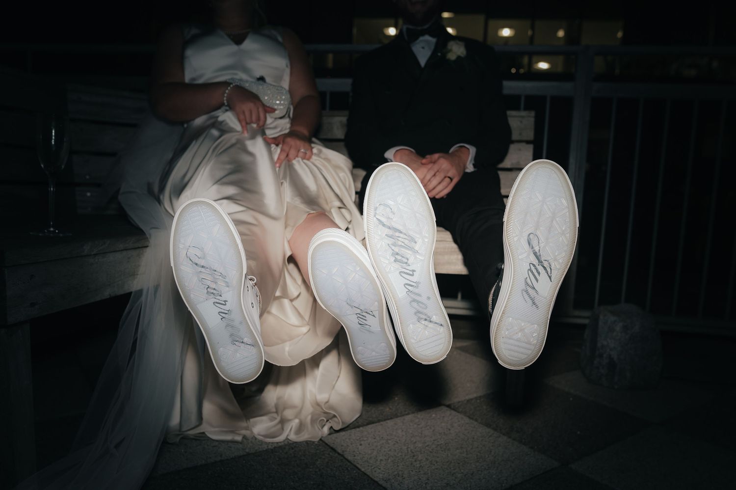 Three pairs of white Nike sneakers lined up showing their soles against a dark background at night.