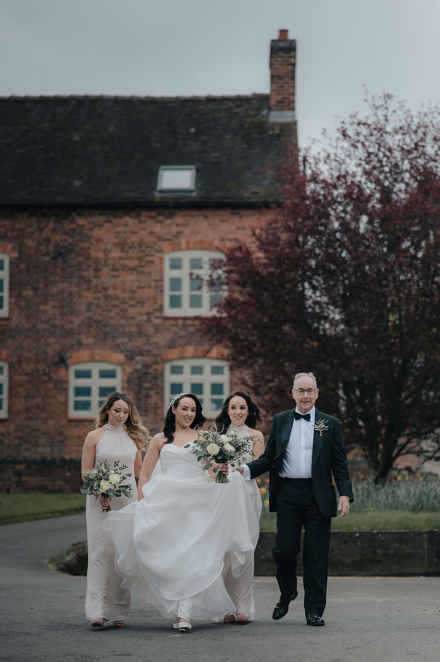 Wedding party walking outside brick building on overcast day.