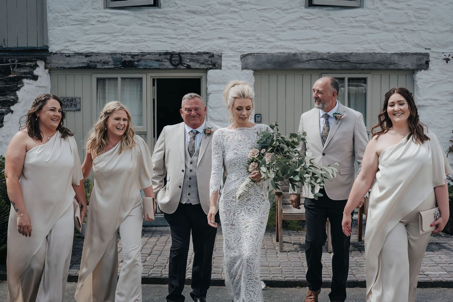 Wedding party in neutral tones posing together outside a white building.