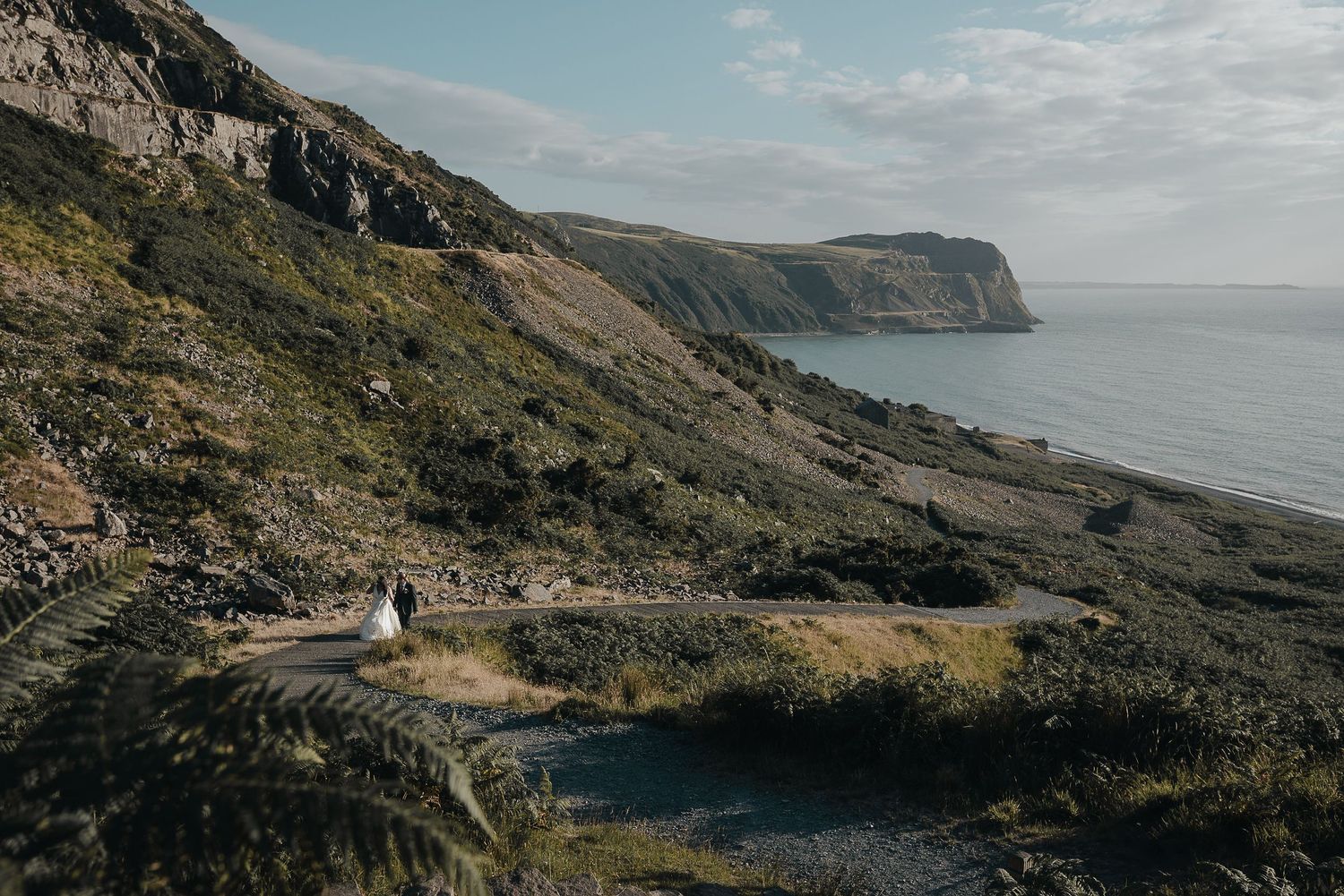 Dramatic coastal cliff landscape with tiny figures visible on hiking path.