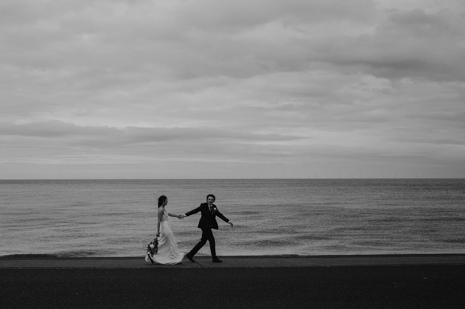 A silhouetted couple dances together on a beach against a moody black and white seascape.