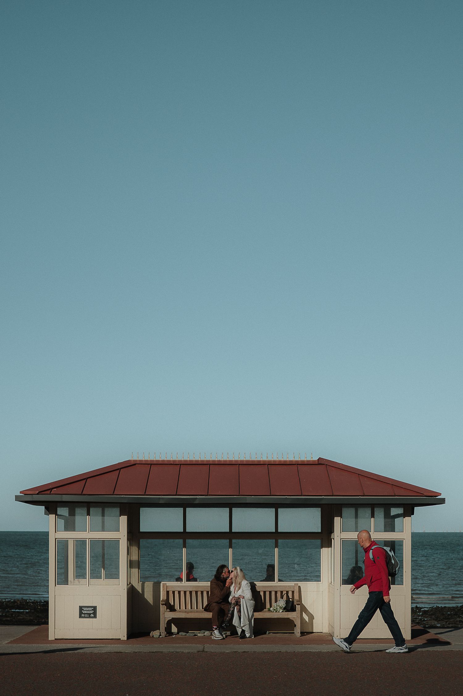 A series of beachside shelter pavilions with red roofs against a blue sky and ocean horizon.
