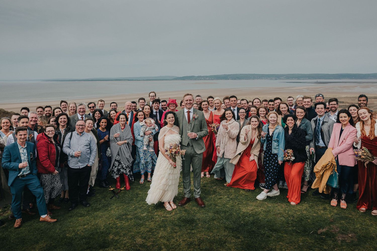 Large group photo of wedding guests gathered on coastal clifftop.