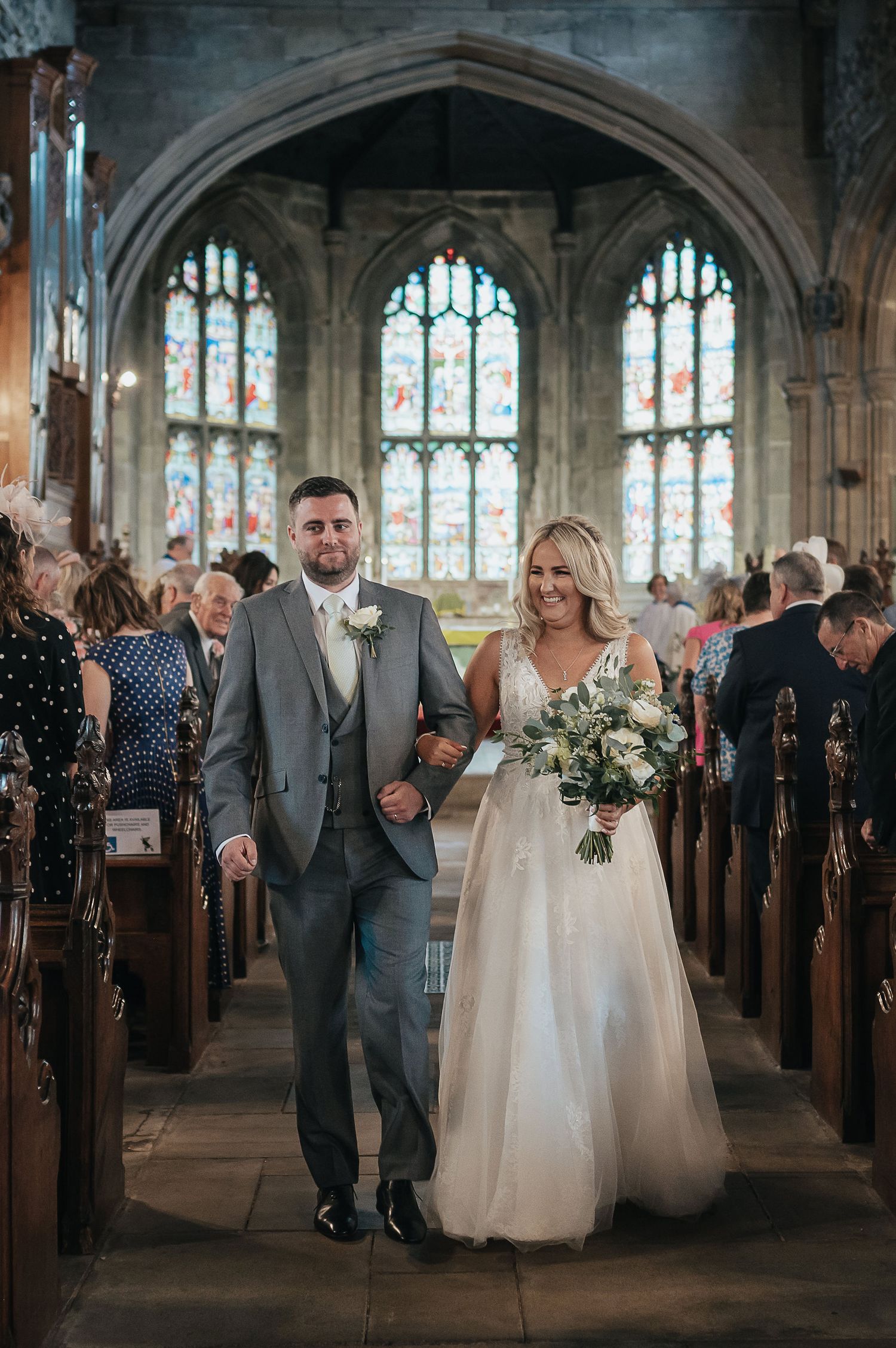Newlyweds walking down the church aisle after their ceremony under ornate stained glass windows.