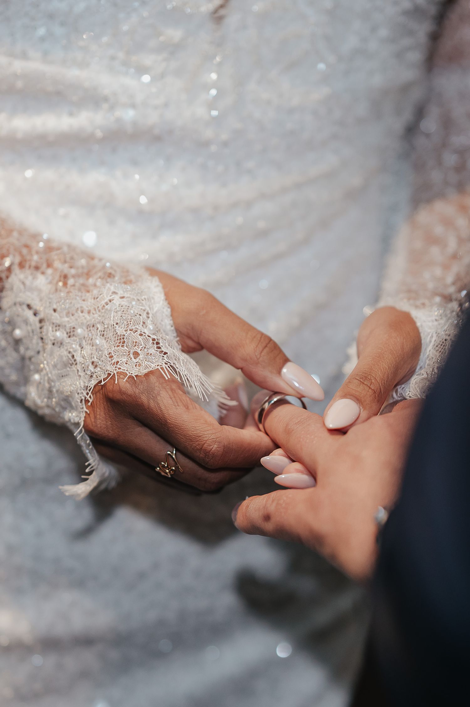 Close-up shot of hands exchanging wedding rings against delicate lace fabric.