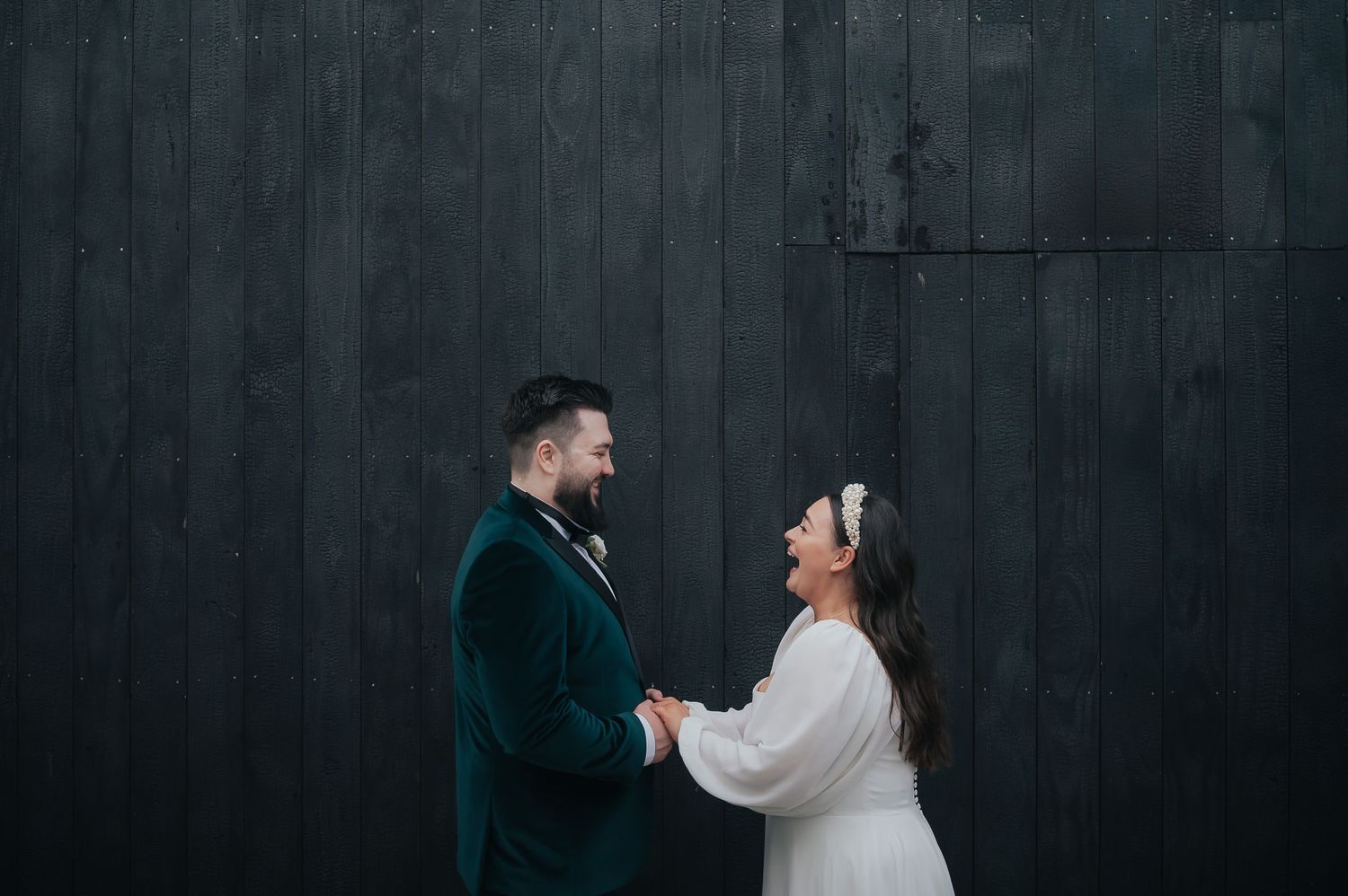 Wedding couple sharing a laugh against dark wooden wall background.