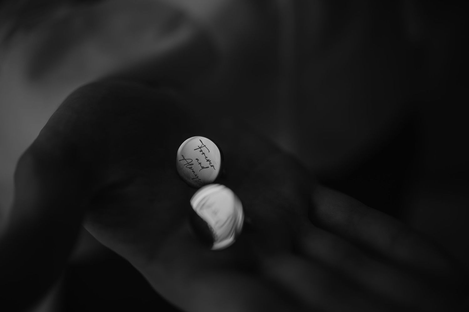 A black and white close-up photograph shows a small coin being held between dark fabric folds.
