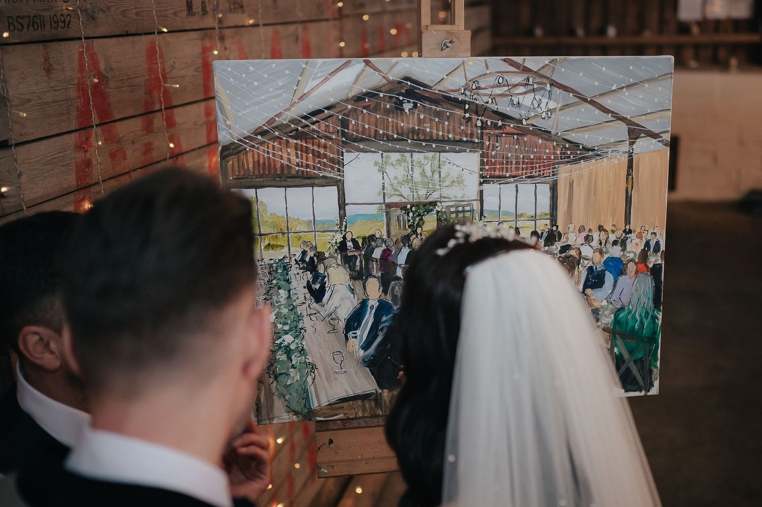 A couple views their wedding venue artwork display with string lights twinkling above.