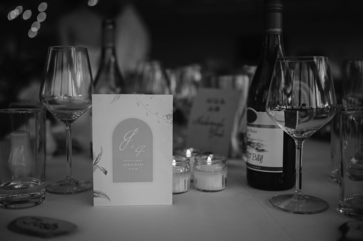 Black and white photo of a wedding reception table setting with wine glasses and menu cards.