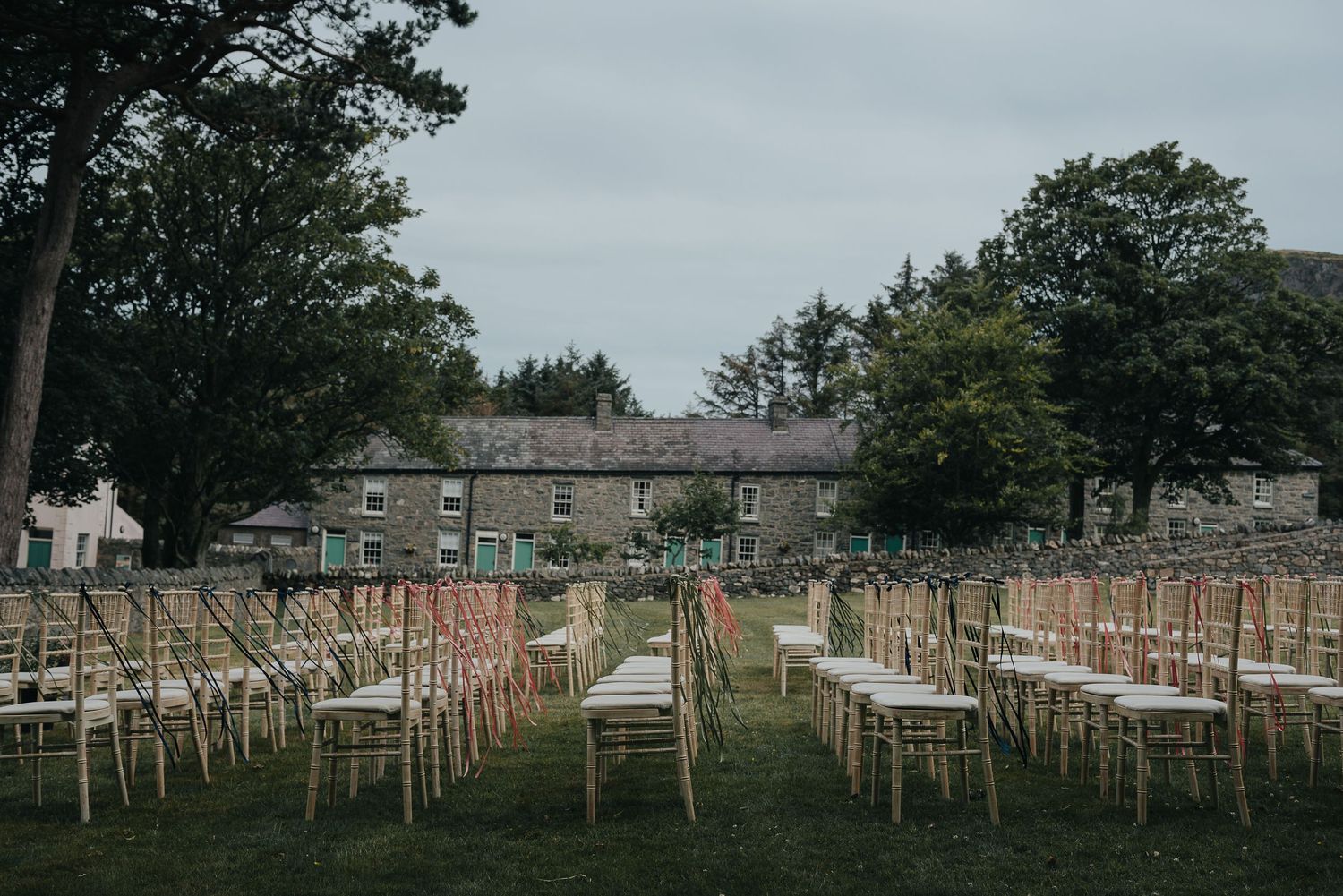 Rows of white chairs set up for an outdoor wedding ceremony at a stone building venue.