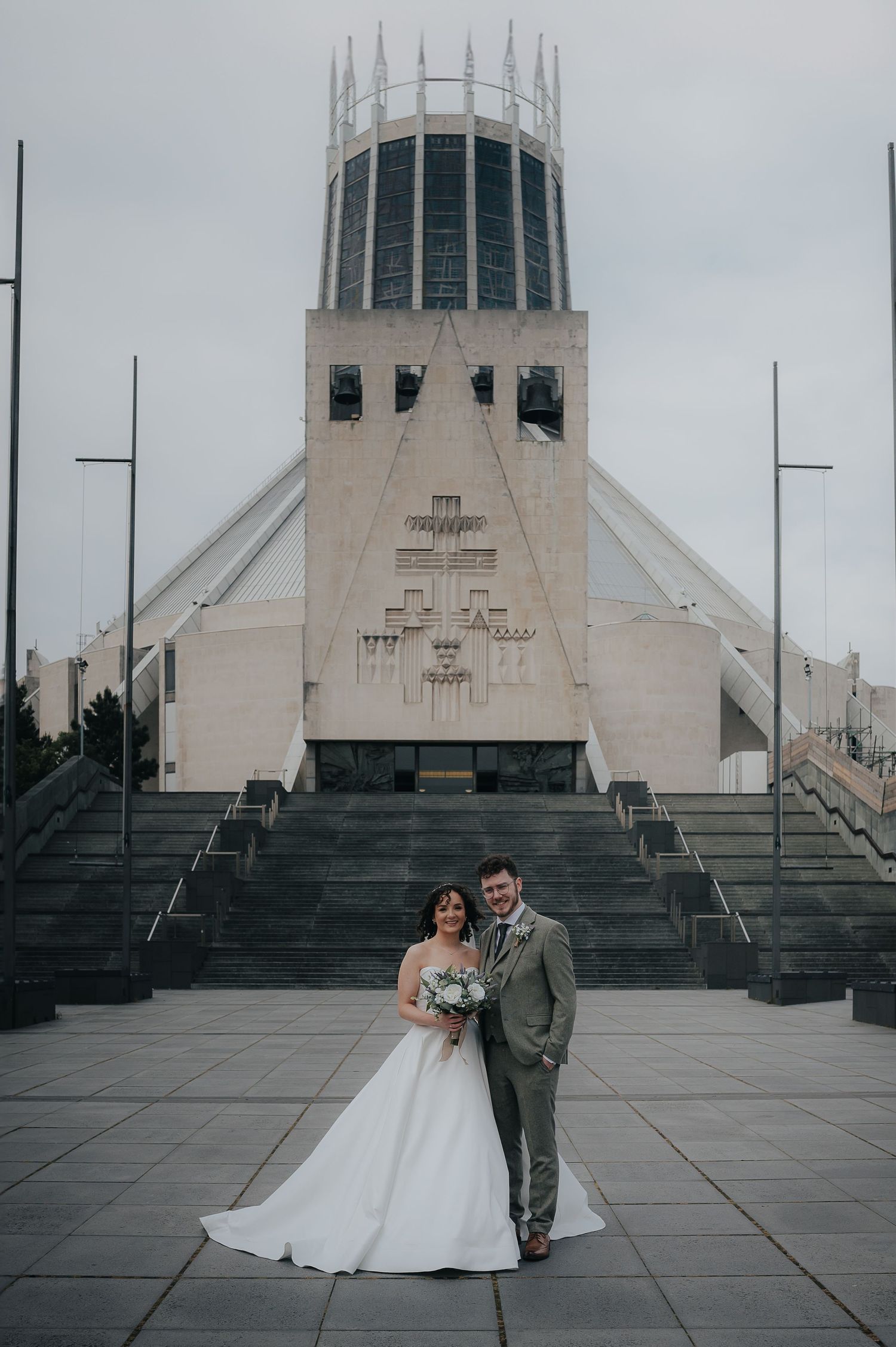 A wedding photo in front of the distinctive architecture of Liverpool Metropolitan Cathedral.