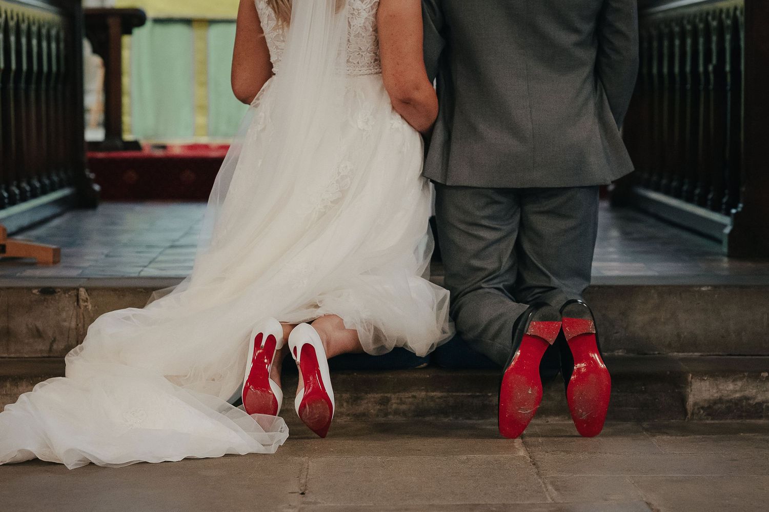 Creative photo showing couple's shoes - white dress and red footwear on church steps.