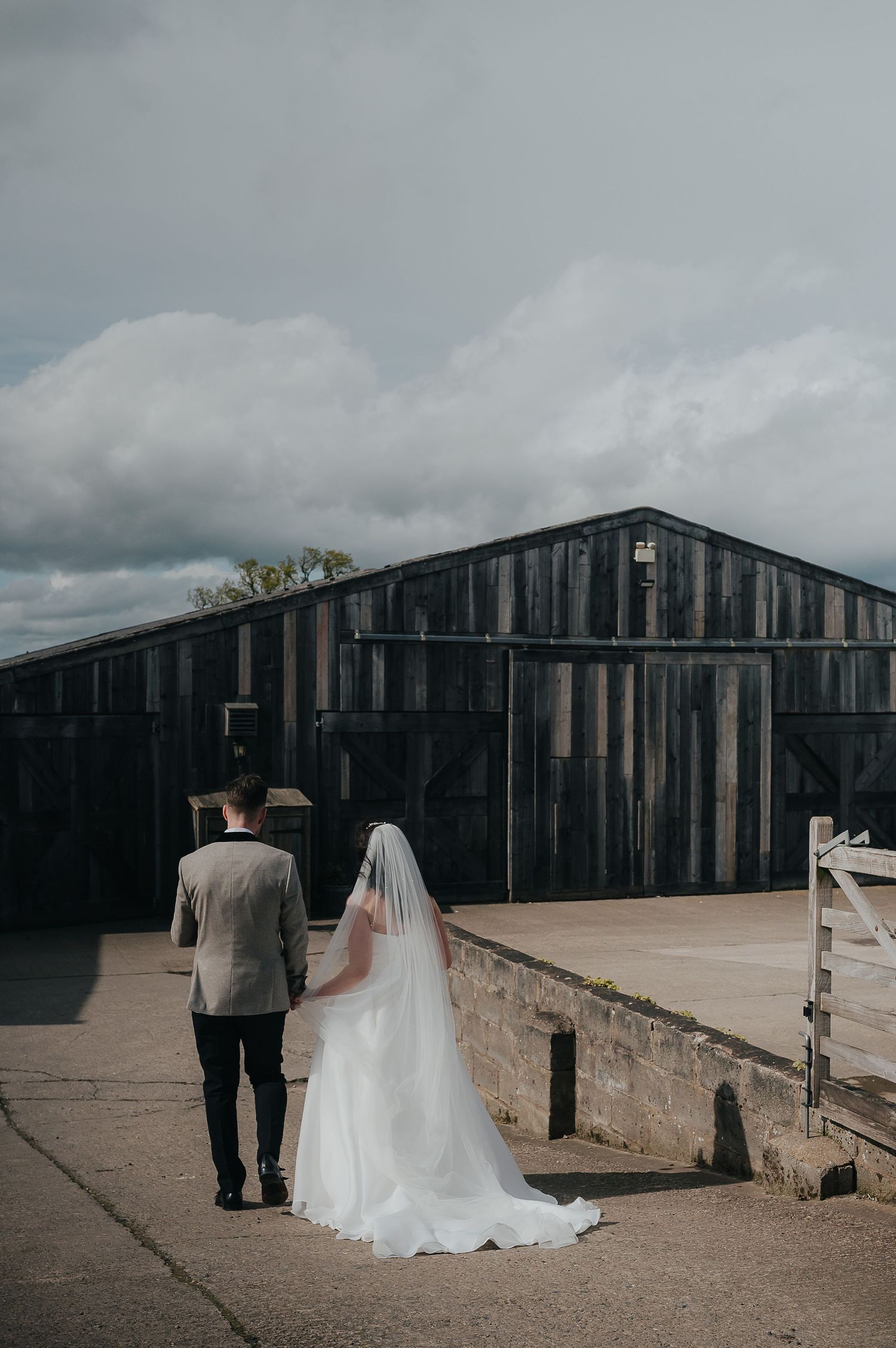 Couple walks hand in hand towards rustic barn wedding venue.