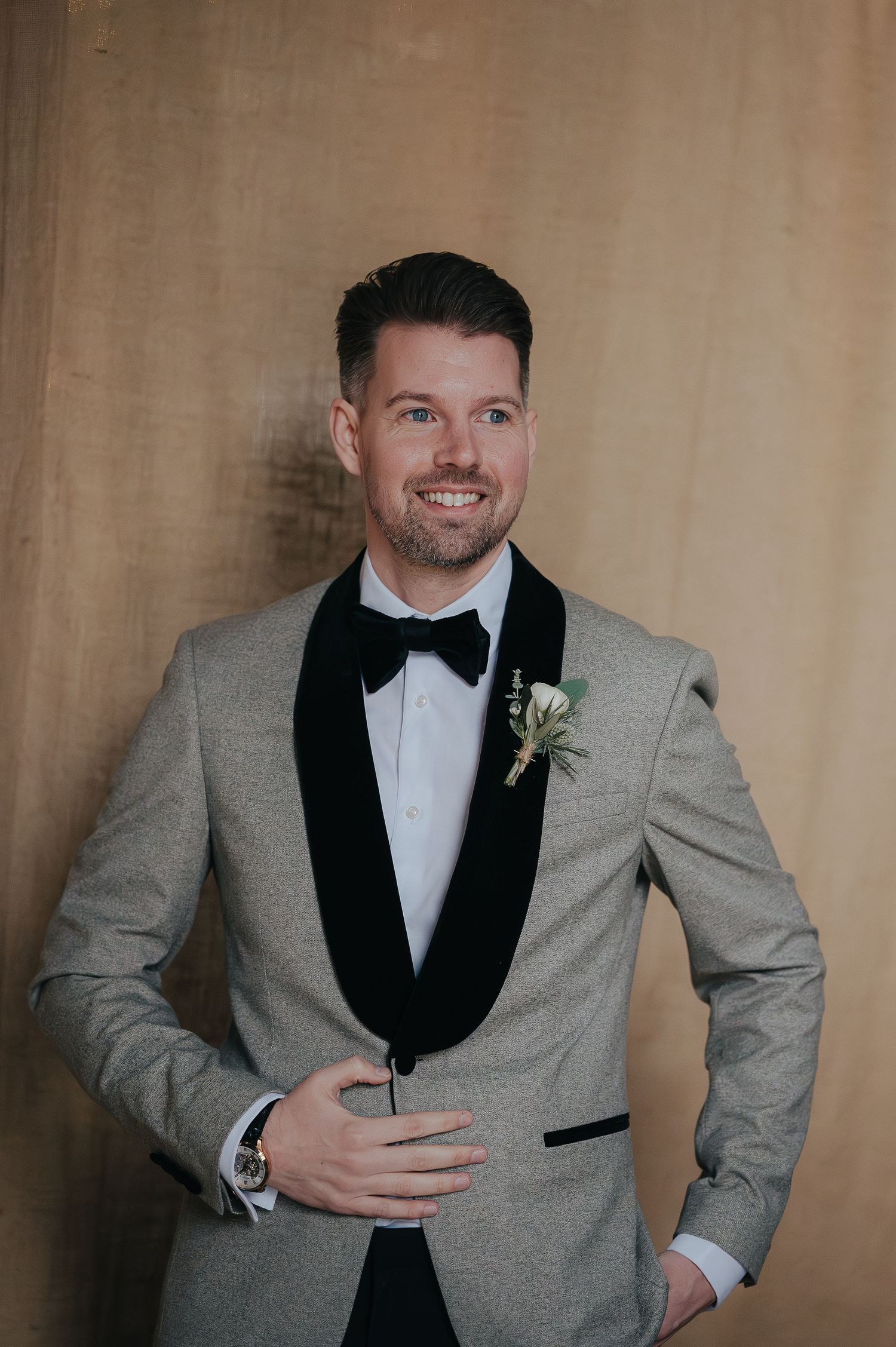 A groom in a light gray tuxedo with black lapels poses for a formal portrait.