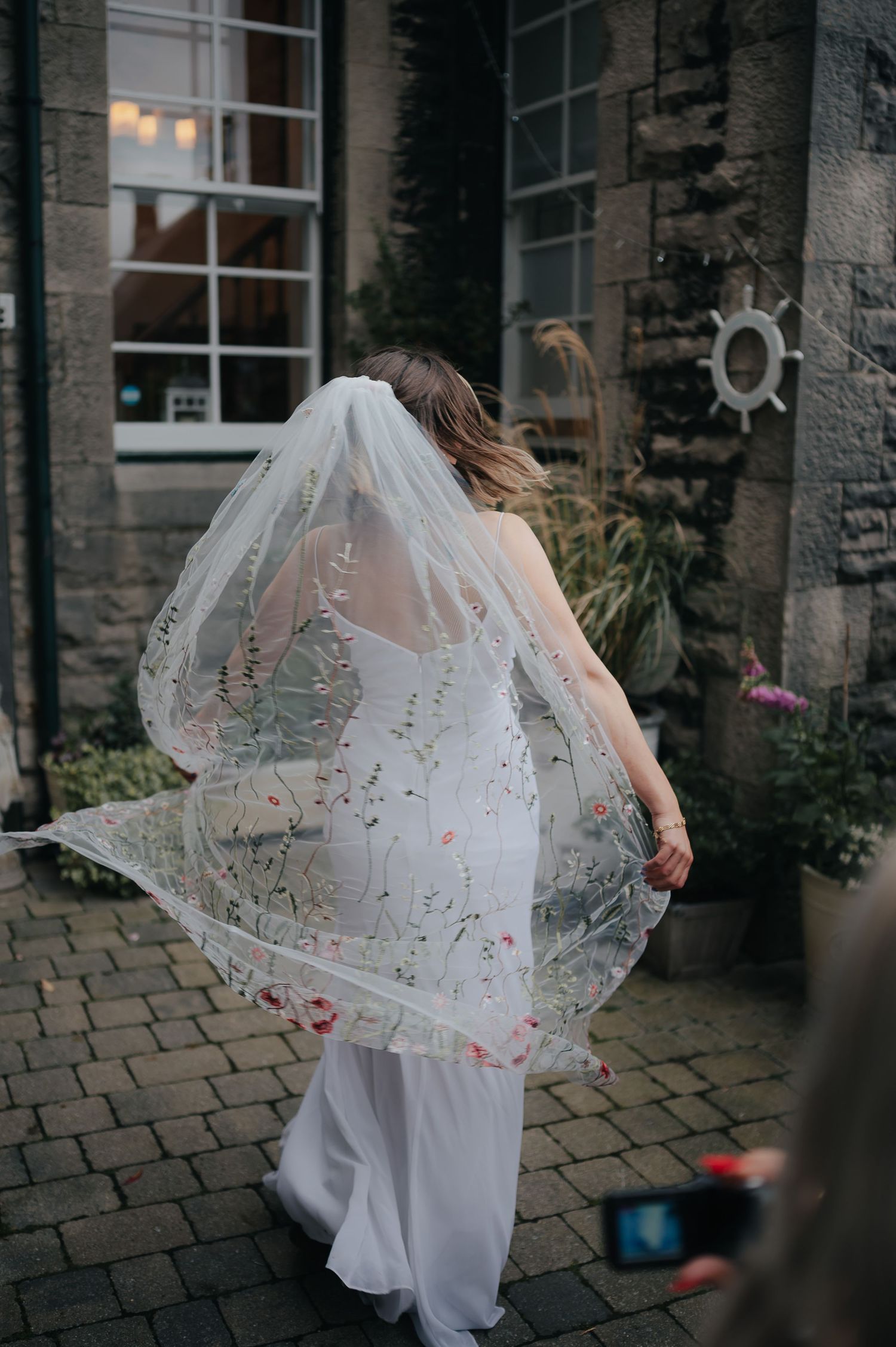 A delicate lace wedding veil flows in the breeze against stone architecture.