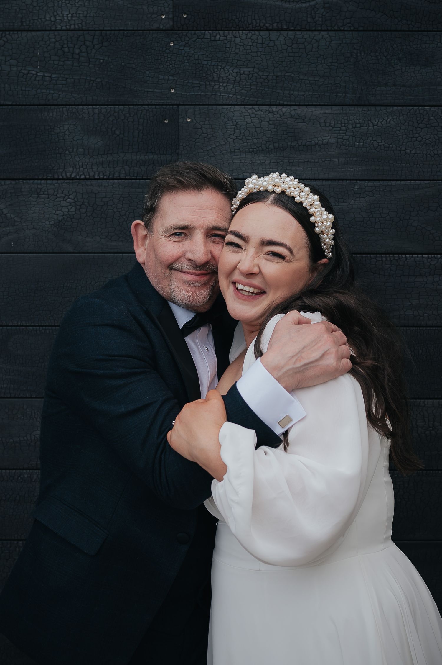 Wedding portrait against a dark wooden wall showing joyful emotions and a pearl crown.
